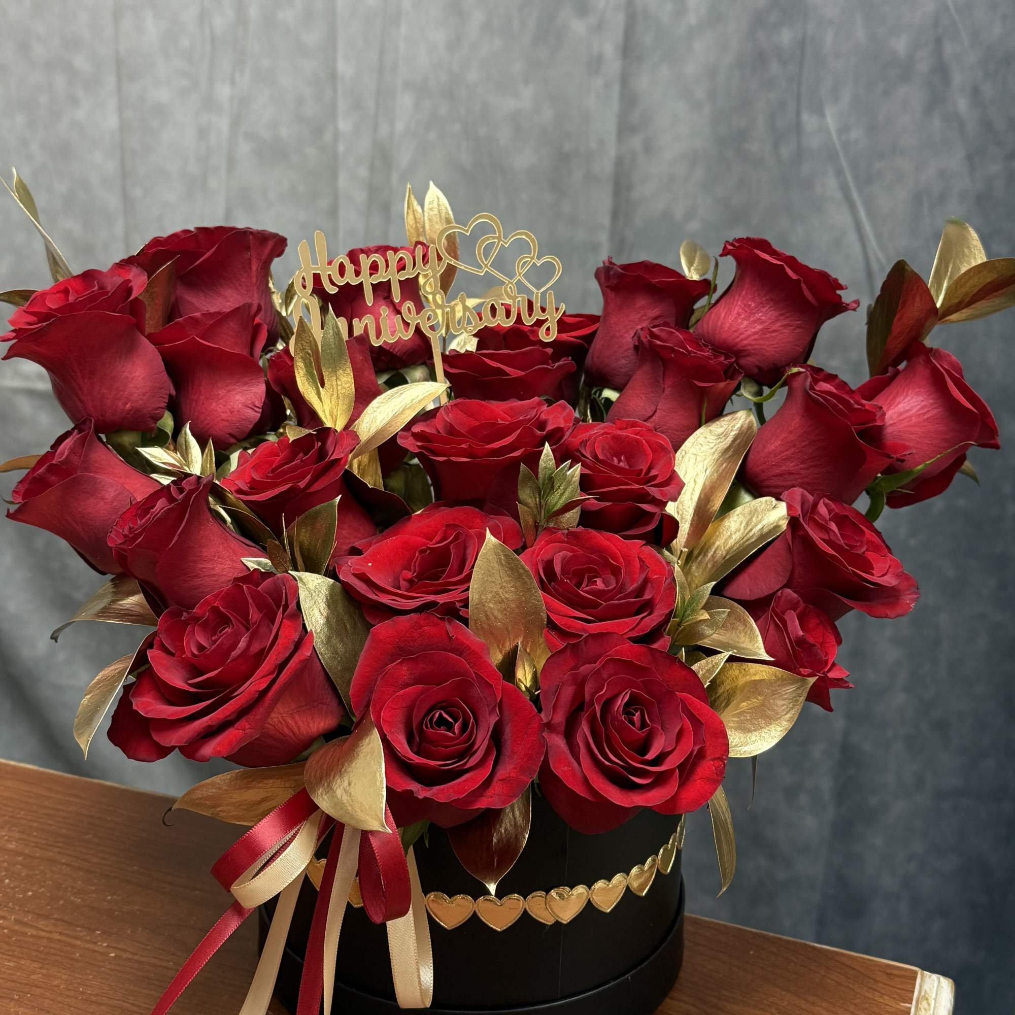 Red roses arranged in a black hat box with a gold anniversary topper