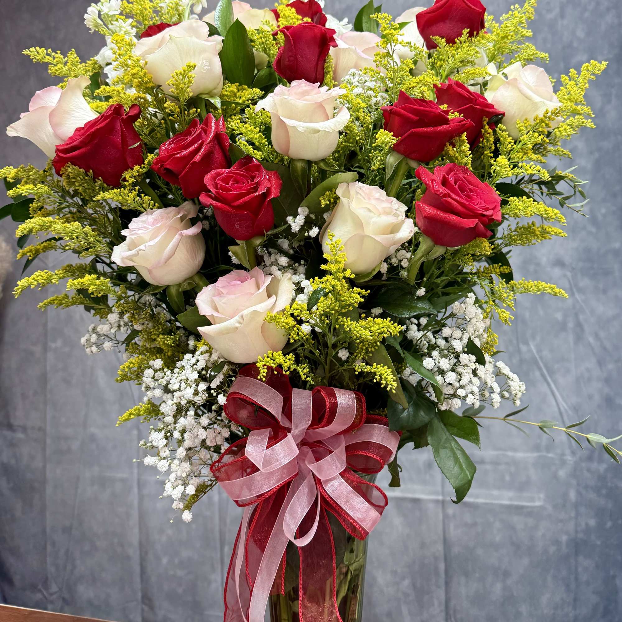 Bouquet of red and white roses in a glass vase with a pink ribbon