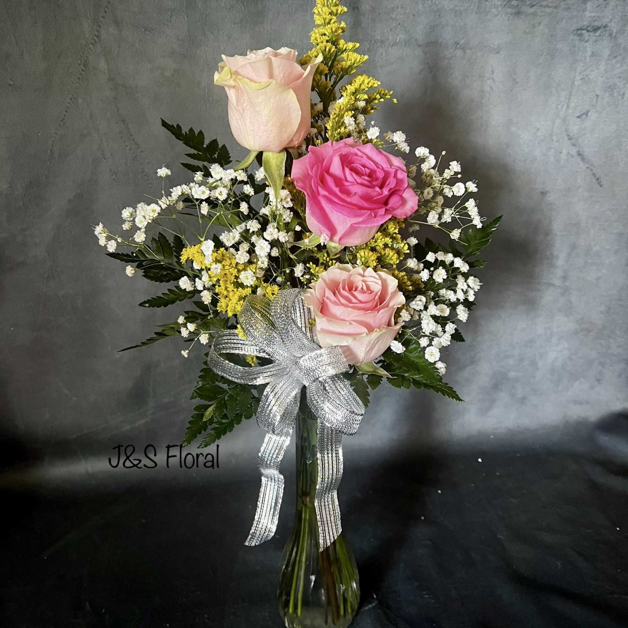 Pink and blush roses in a glass vase with baby's breath and a silver bow