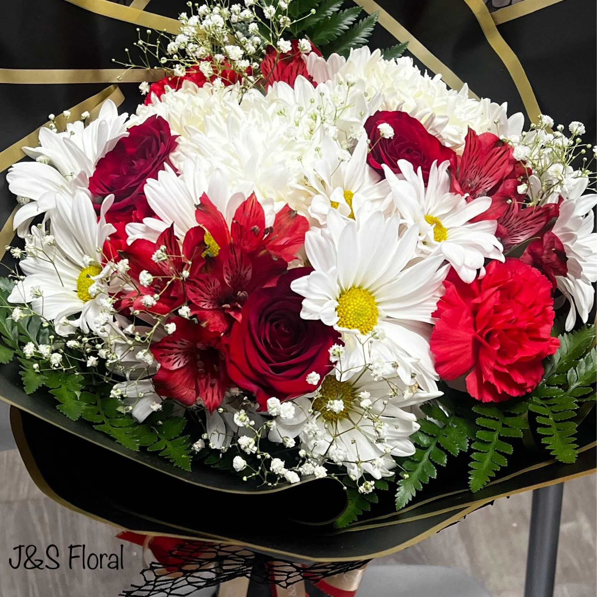 Bouquet of red roses, white daisies, and red carnations wrapped in black paper
