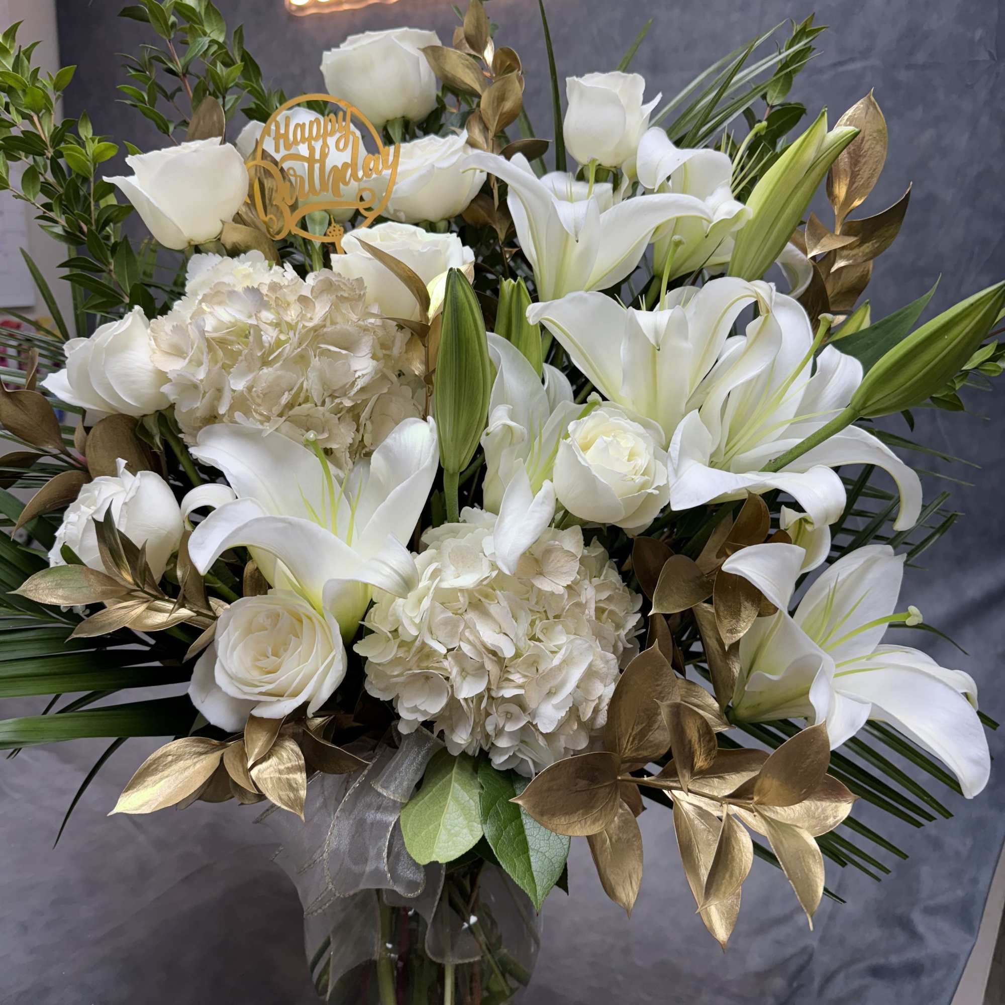 White lilies and roses in a glass vase with a birthday topper