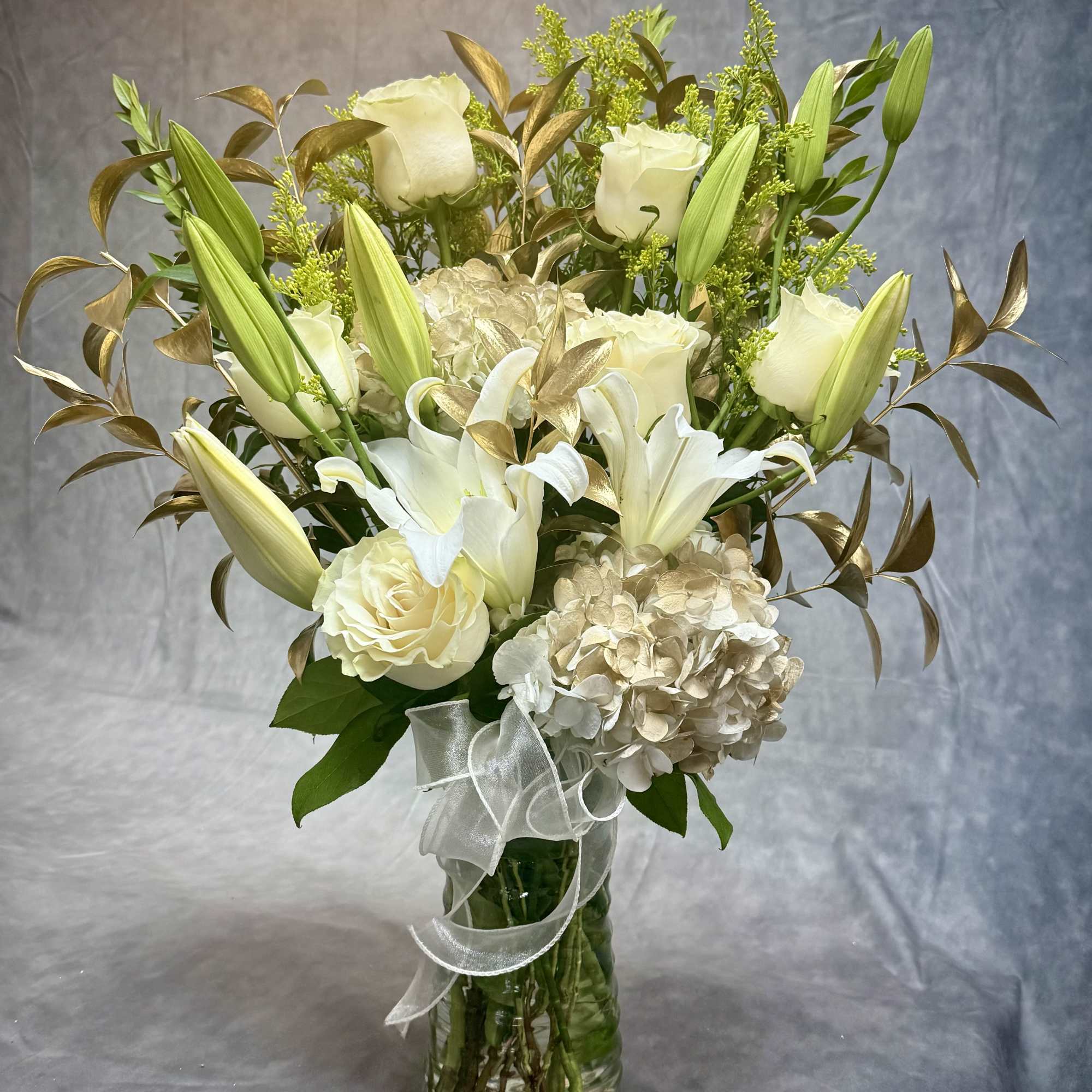White lilies and roses arranged in a glass vase with a ribbon