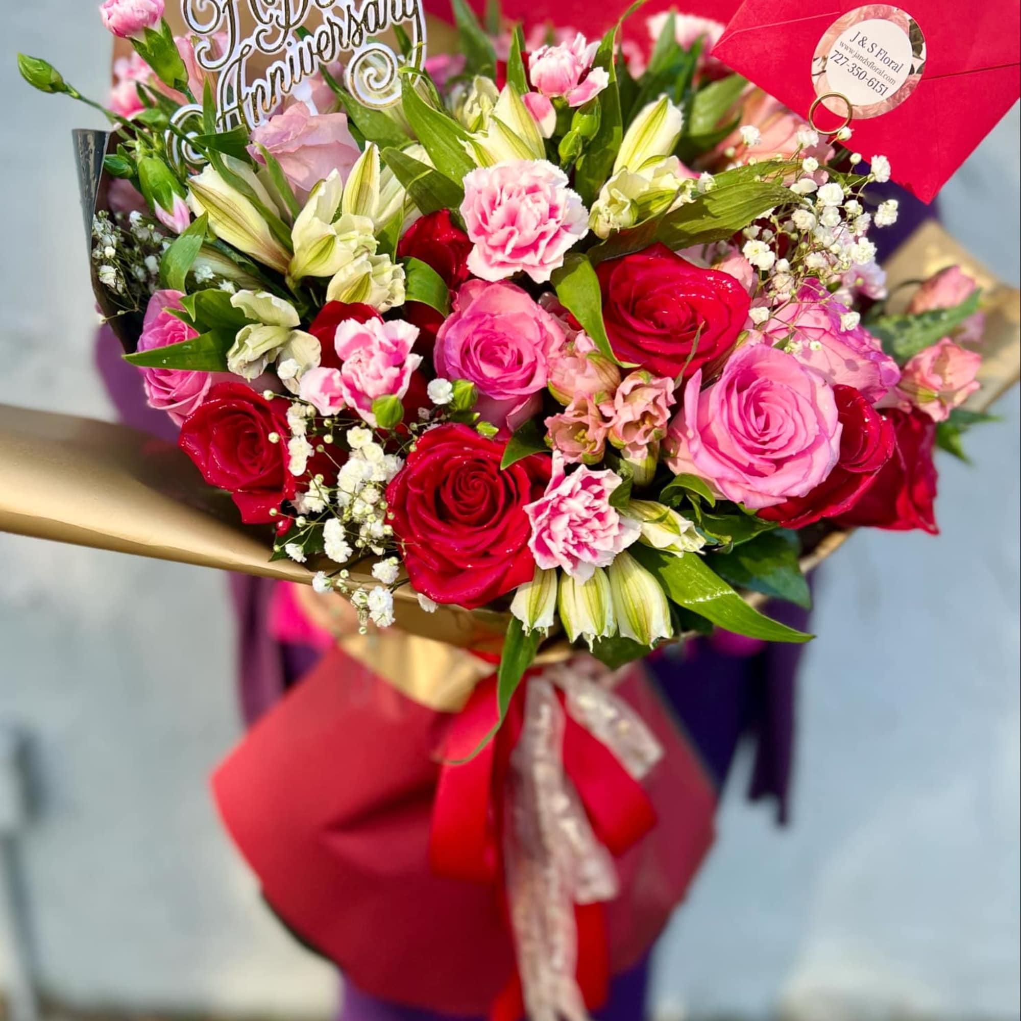 Bouquet of pink and red roses with lilies and carnations, wrapped in red paper