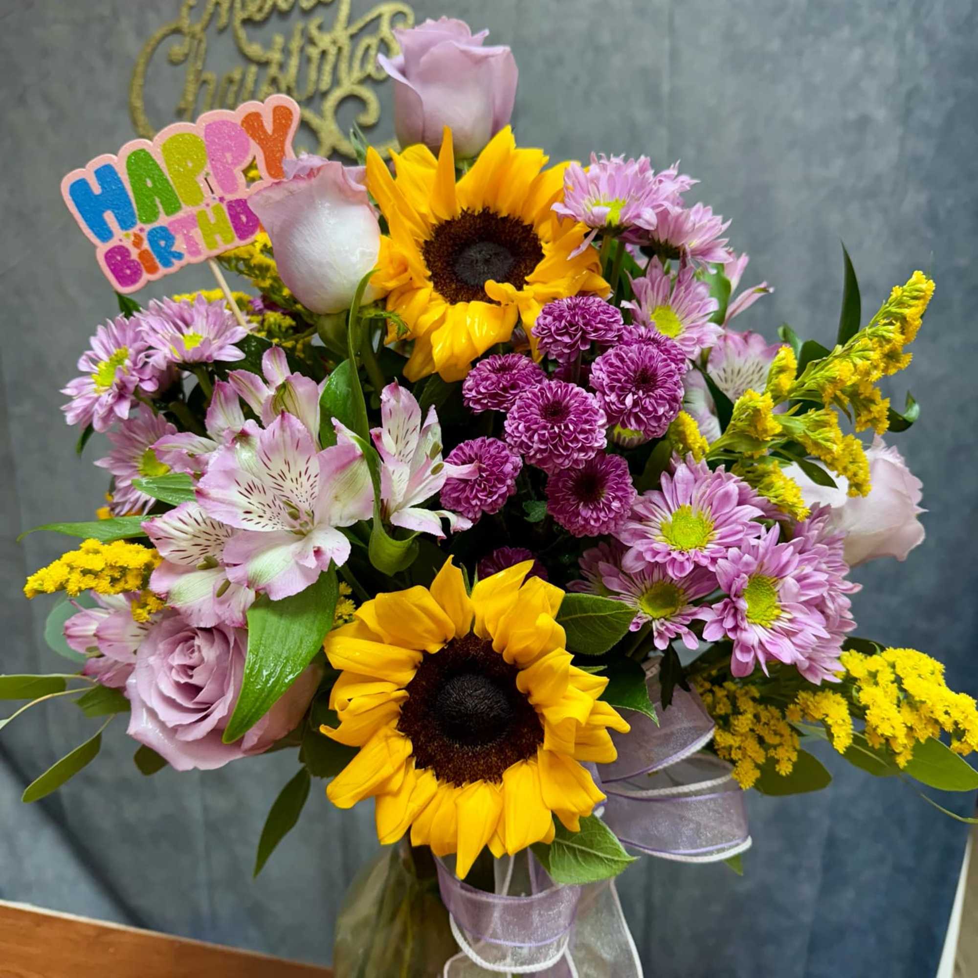 Mixed bouquet with sunflowers, pink roses, and purple daisies in a glass vase