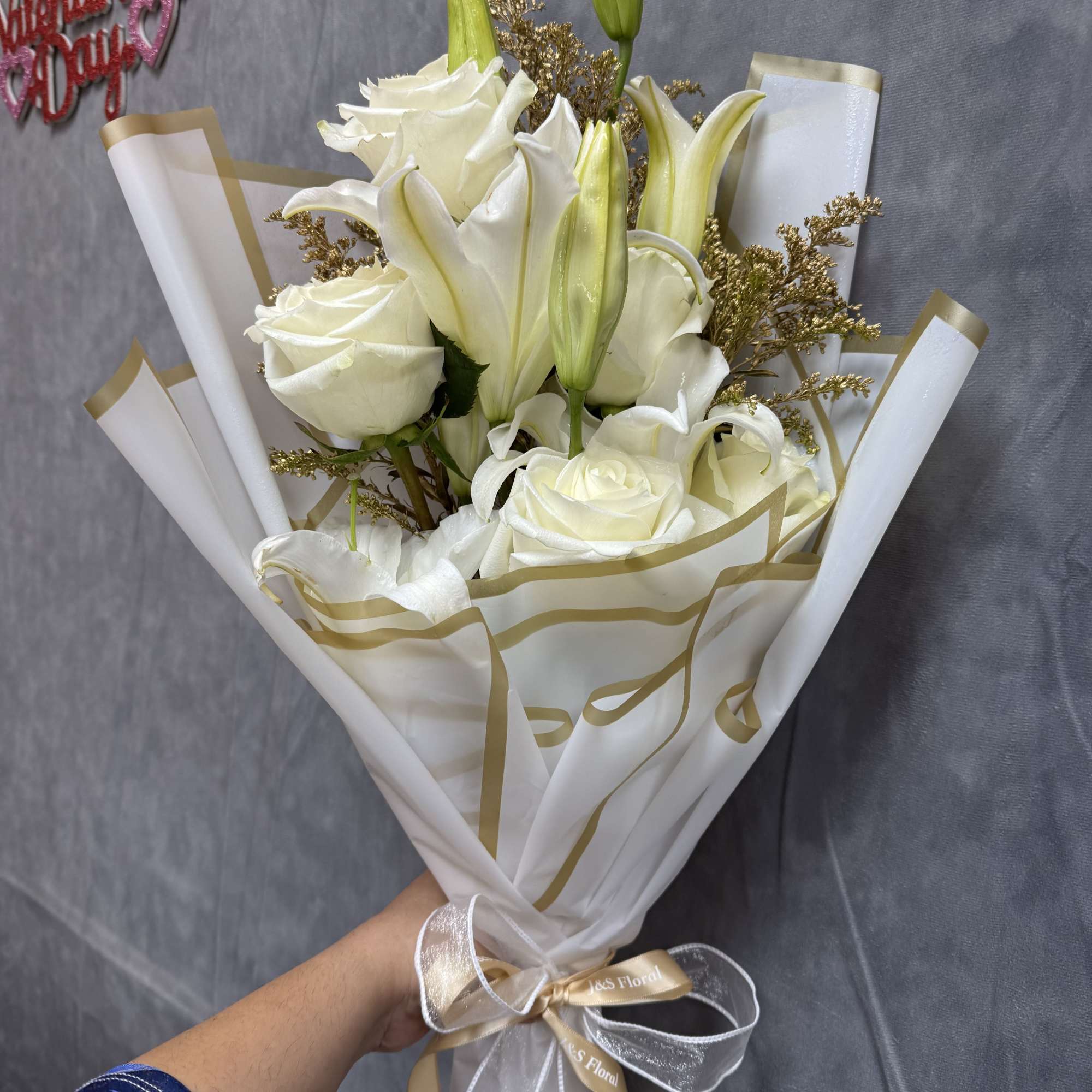 White roses and lilies in wrapped bouquet with gold ribbon