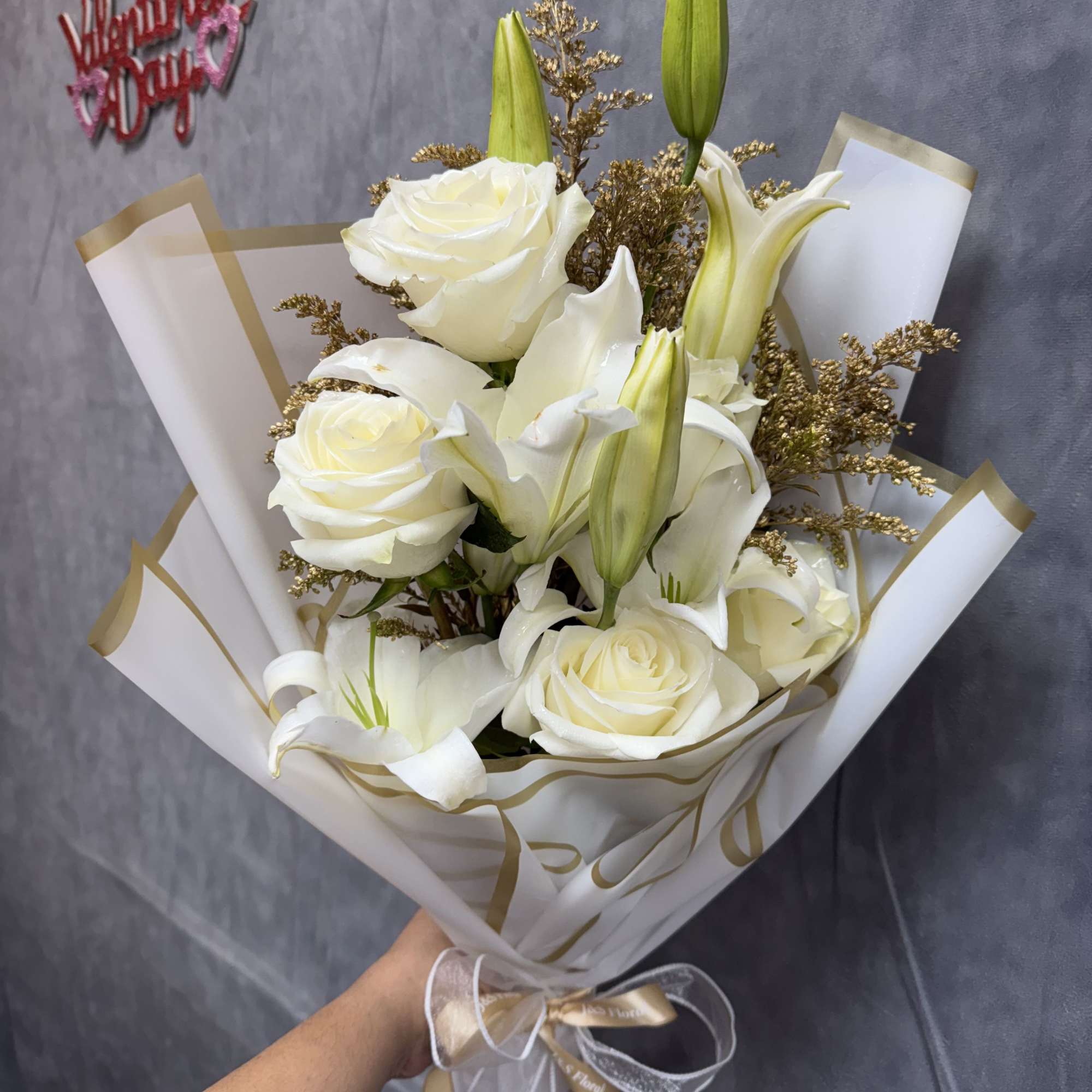White roses and lilies in a wrapped bouquet with gold accents