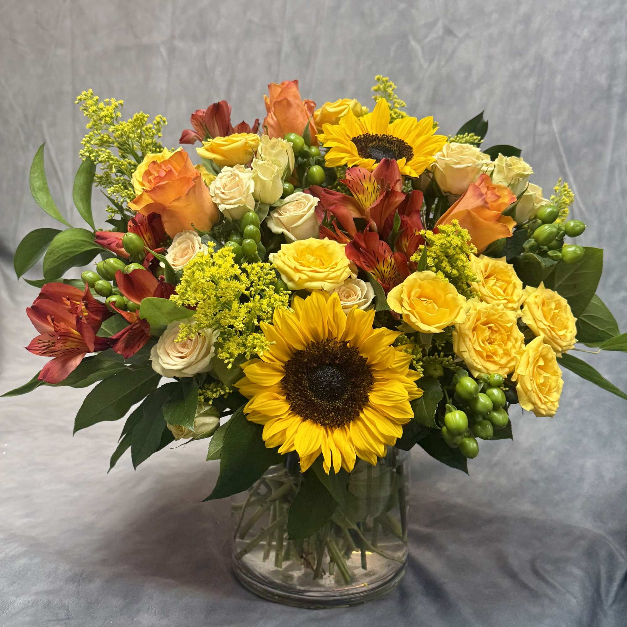 Bouquet of sunflowers, roses, and orange alstroemeria in a glass vase