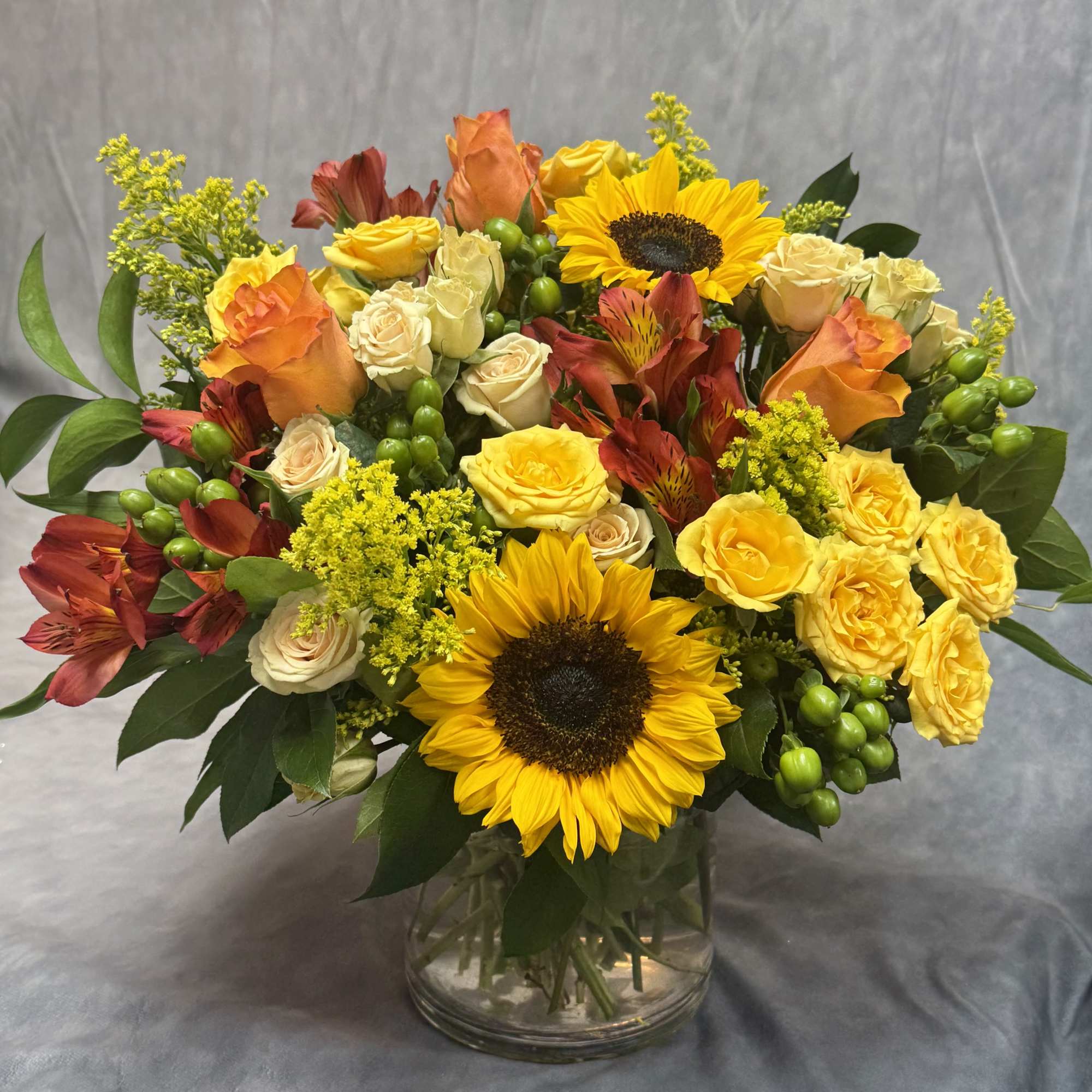 Bouquet of yellow sunflowers, roses, and red alstroemeria in a glass vase