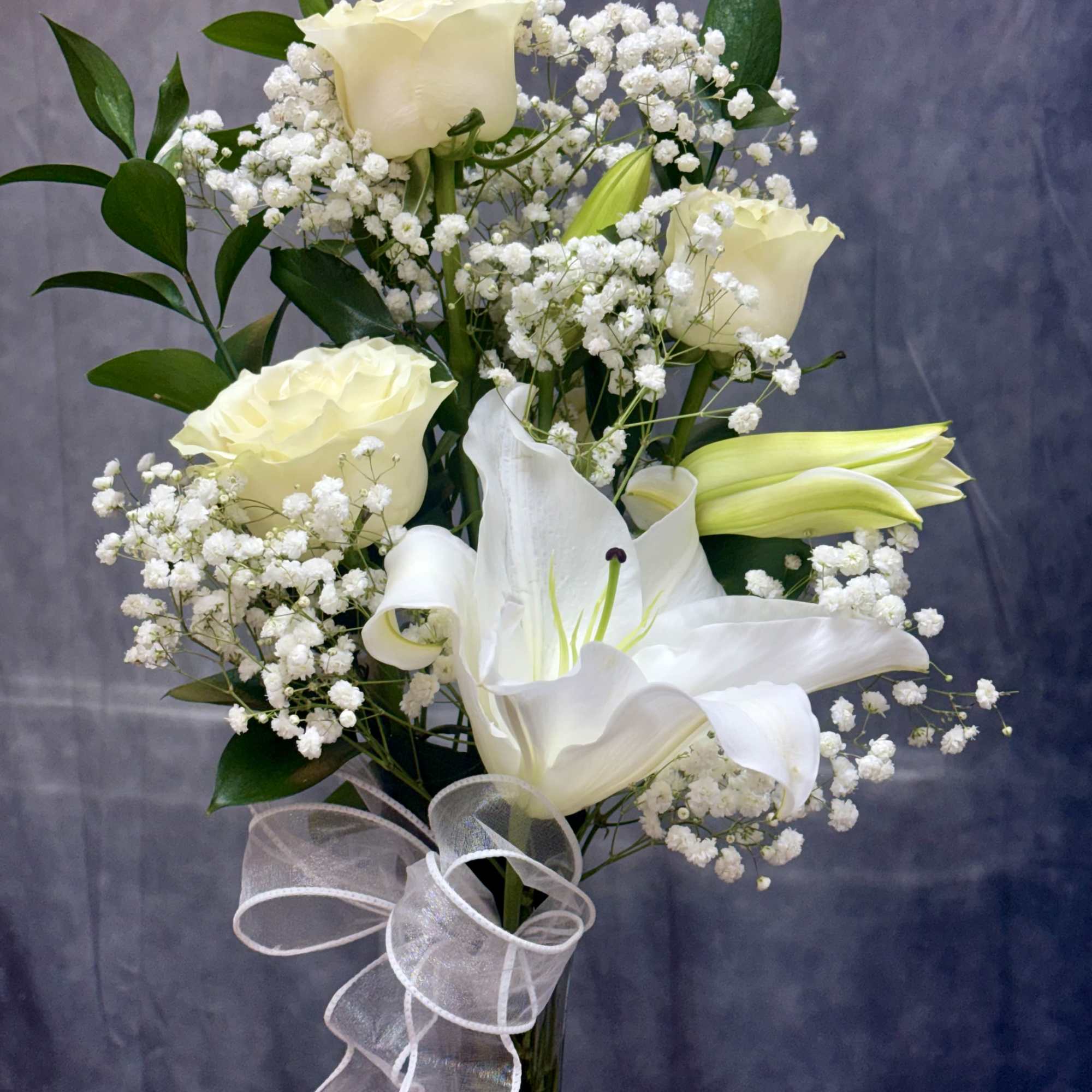 White roses and lilies arranged with baby's breath and a sheer ribbon.