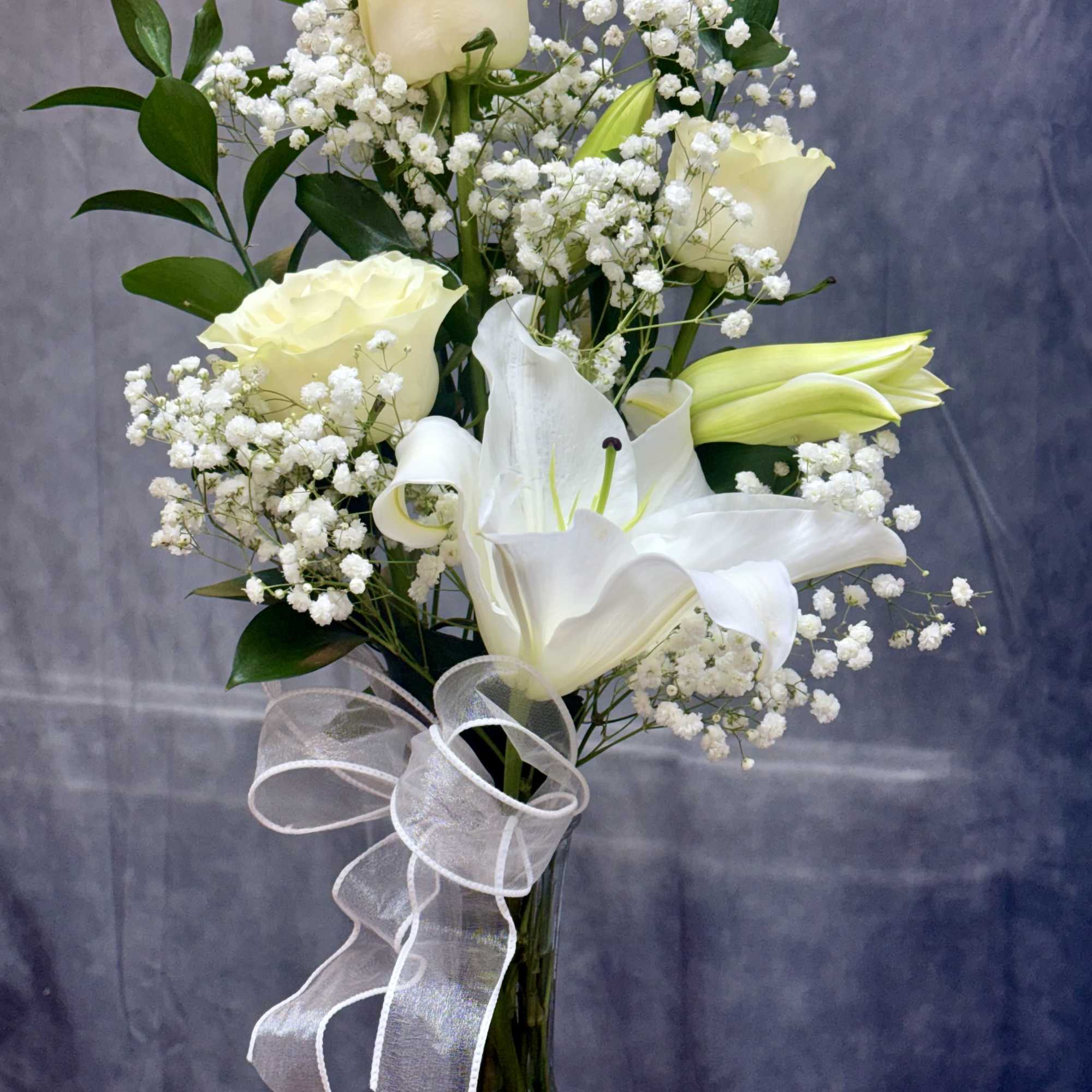 White roses and lilies arranged in a tall glass vase with a sheer ribbon.