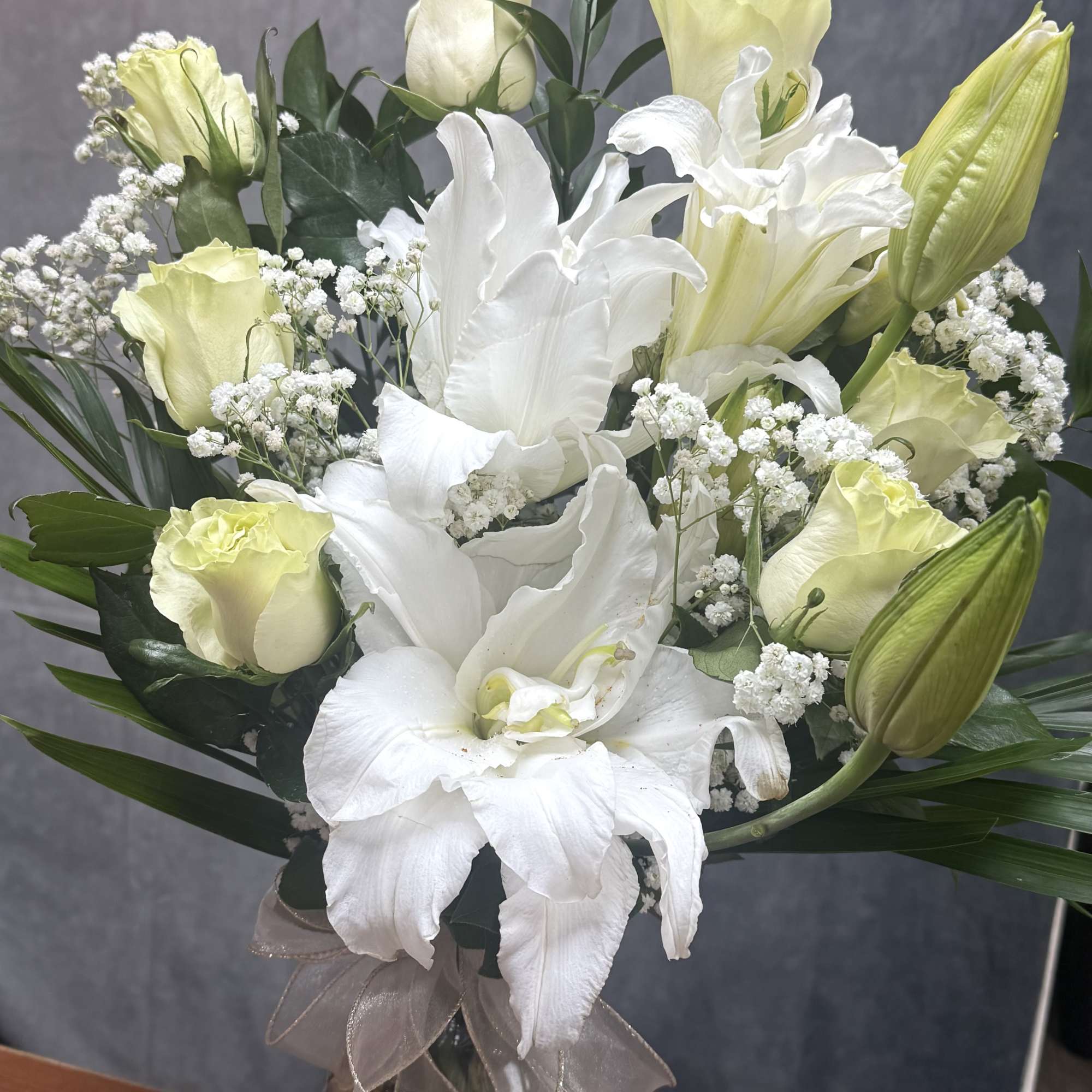 White lilies and pale yellow roses in a glass vase with a ribbon.