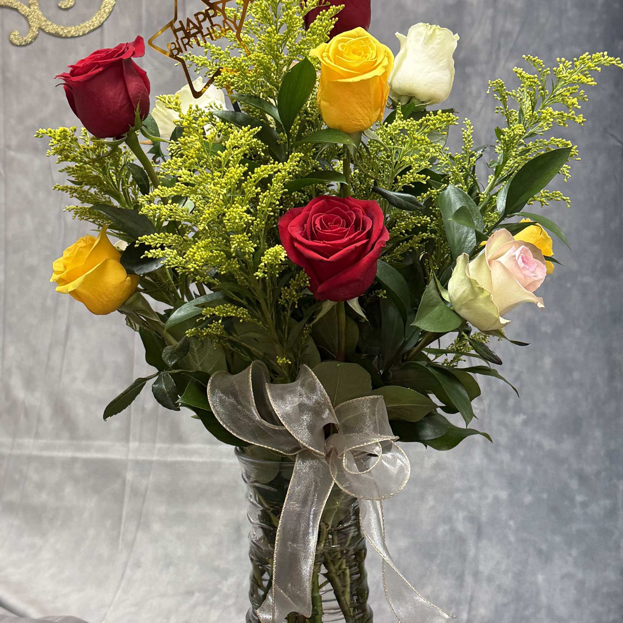 Bouquet of red, yellow, and white roses in a glass vase with a ribbon