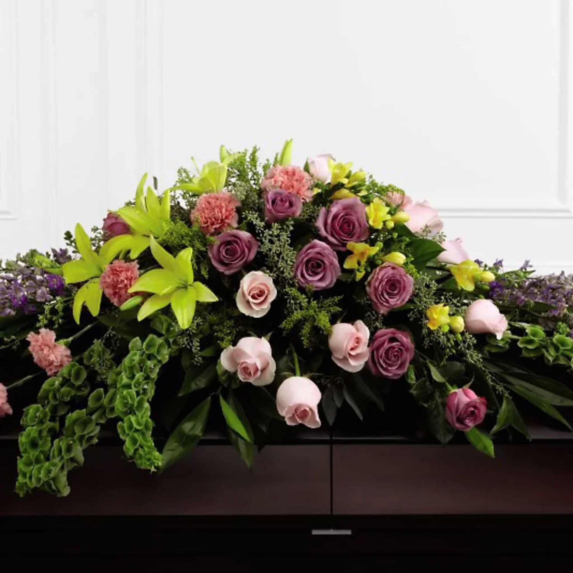 Casket spray with purple and pink roses and green lilies