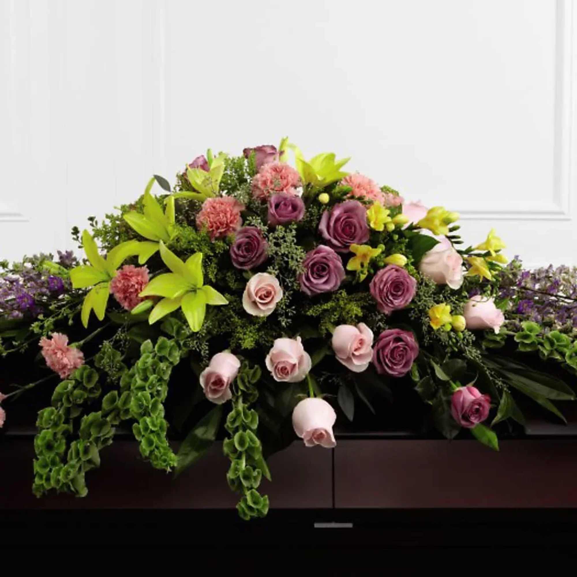 Casket spray with pink and purple roses and green lilies
