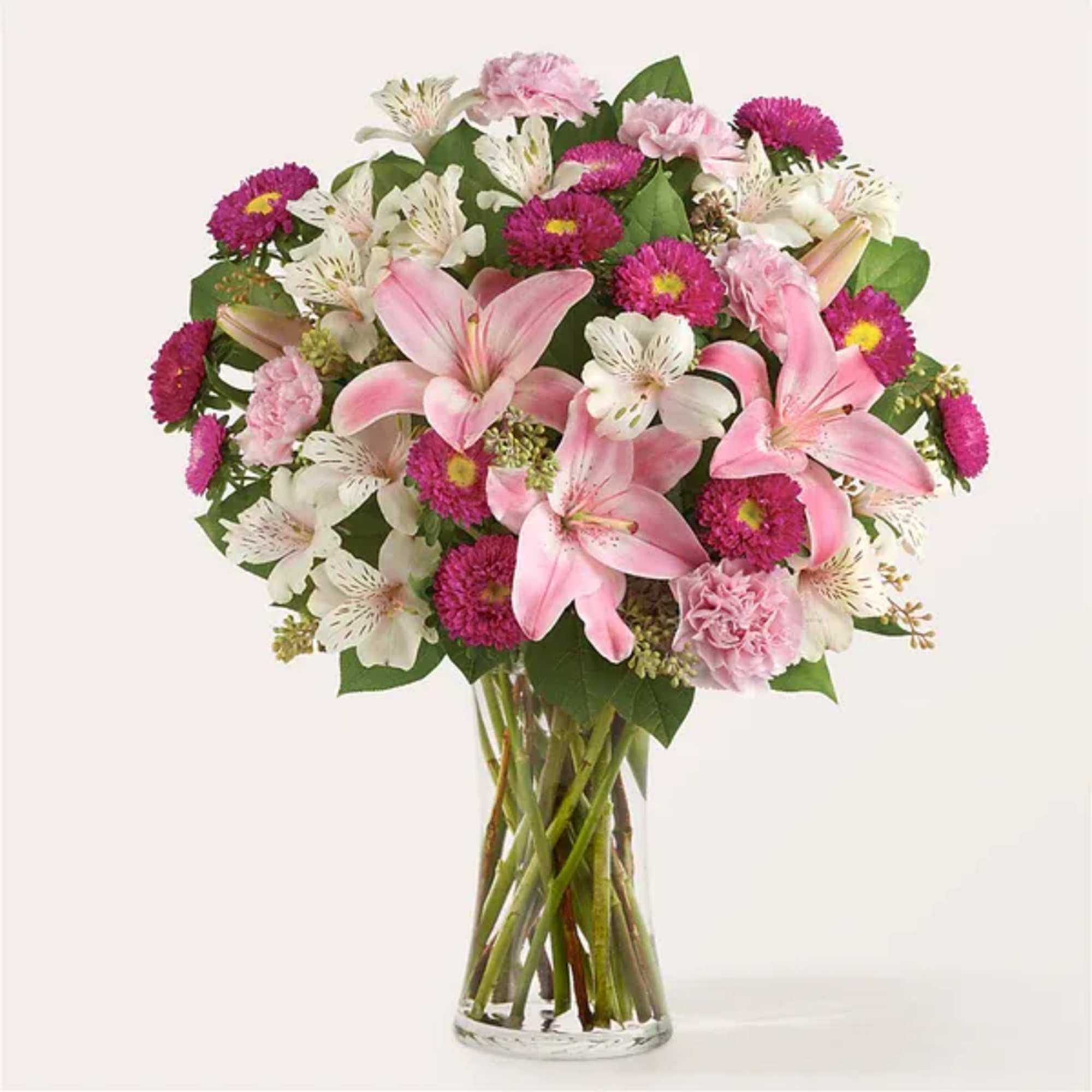 Pink lilies and mixed blooms arranged in a clear glass vase