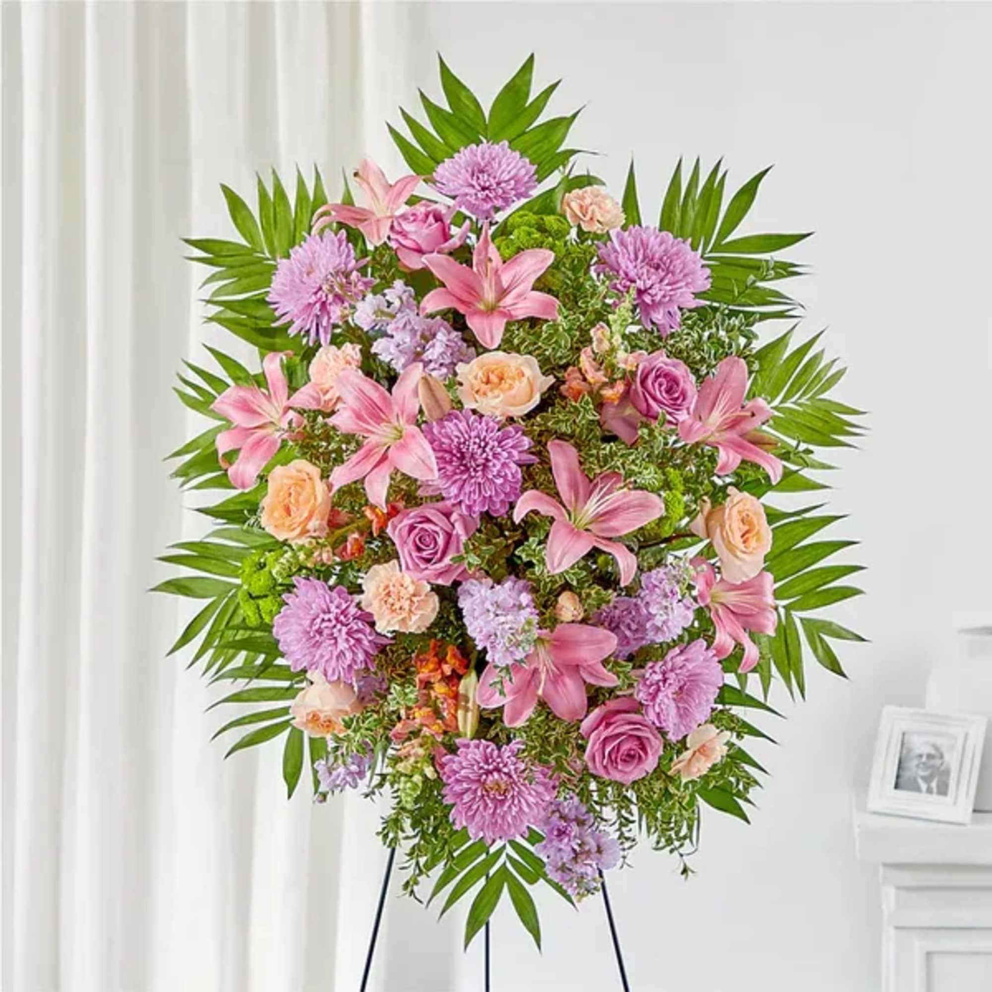 Pink and lavender funeral spray on a stand with lilies and roses