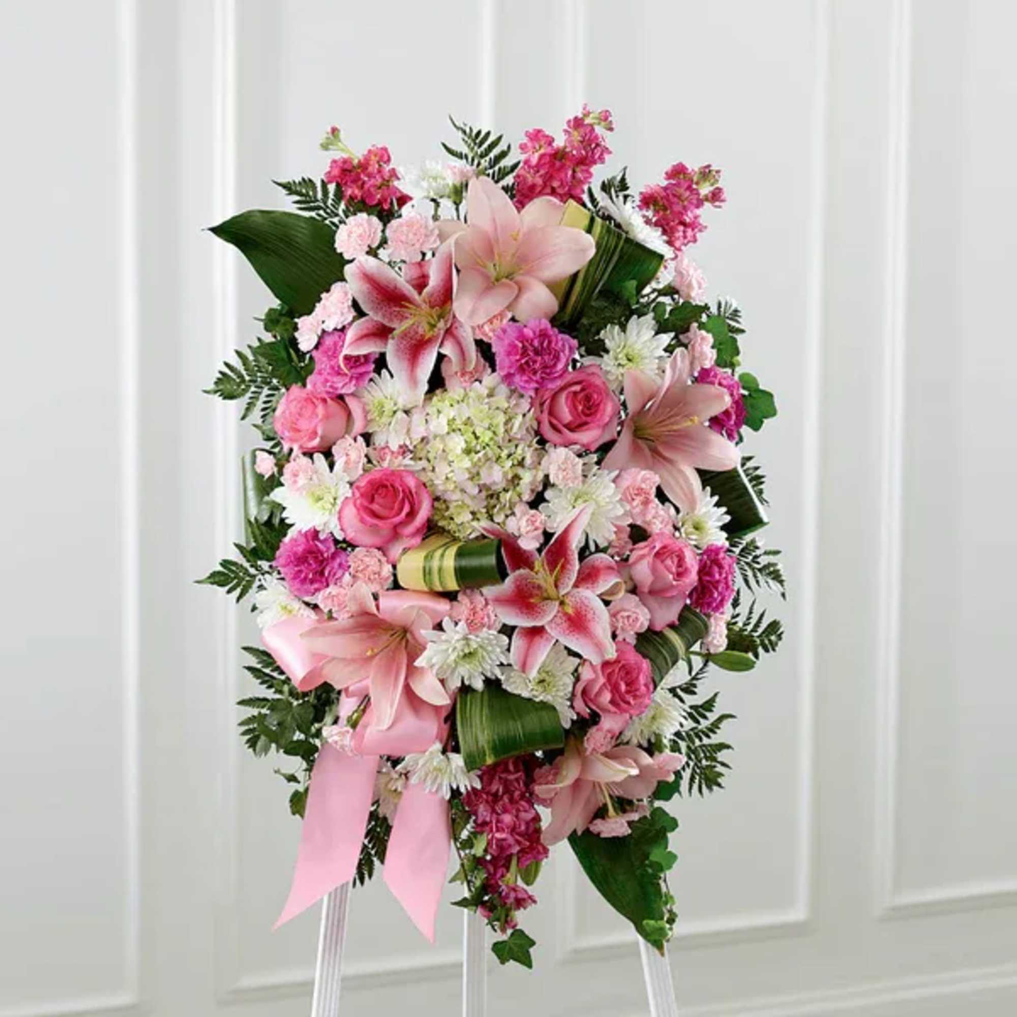 Pink floral standing spray with lilies, roses, and a ribbon on an easel