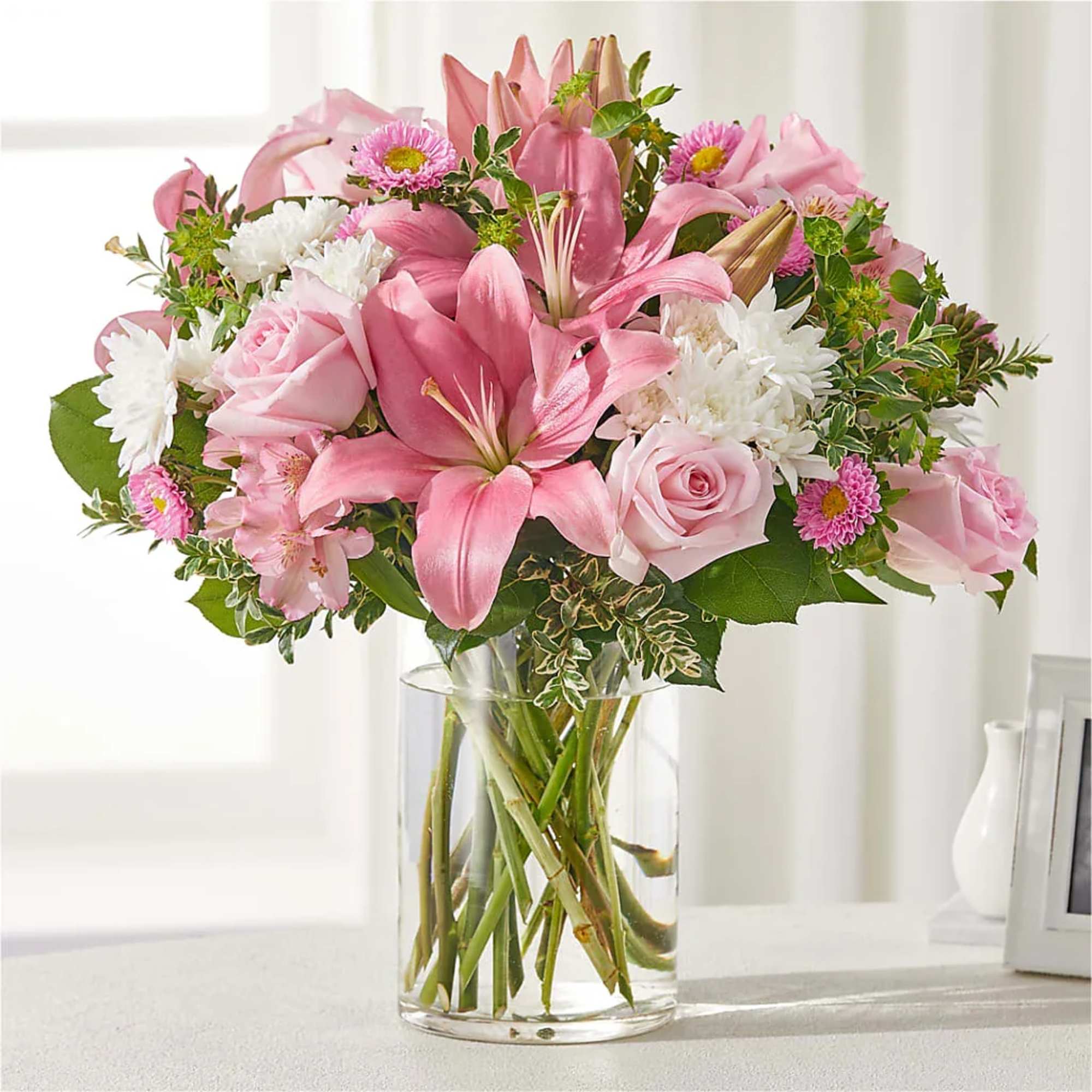 Pink lilies and roses arranged in a clear glass vase