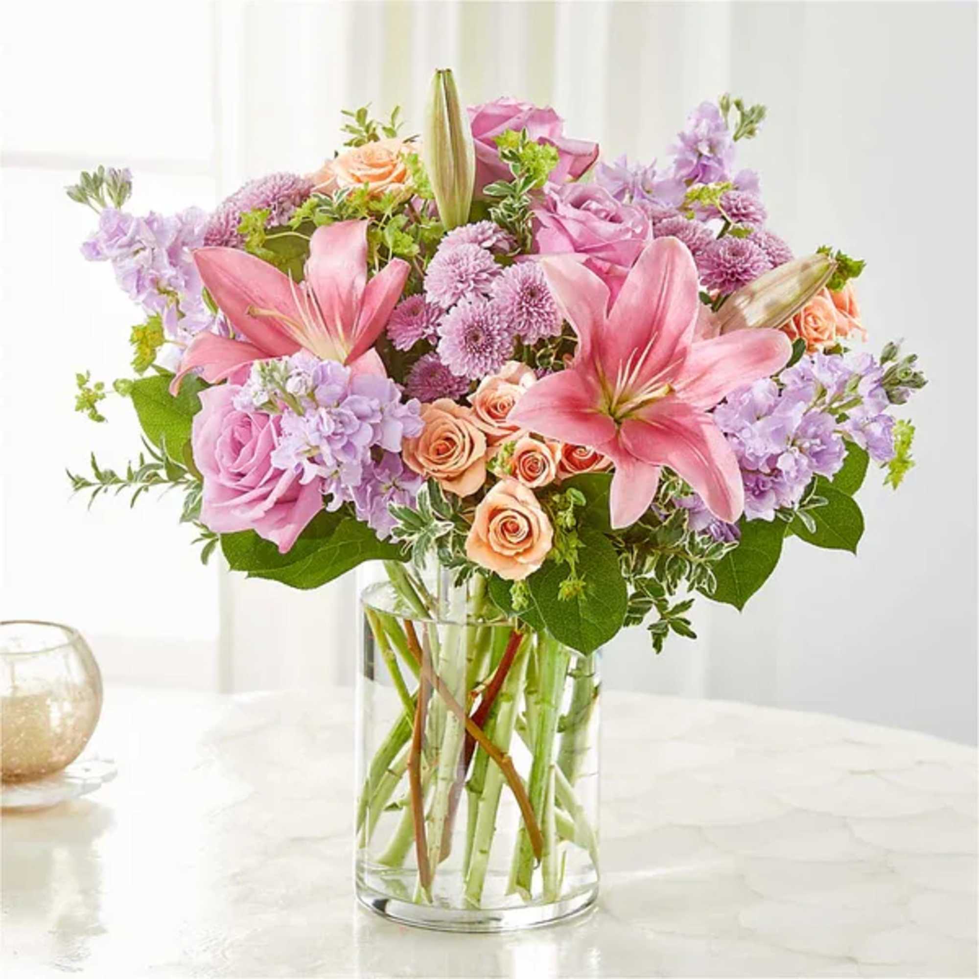 Pink lilies and roses arranged in a clear glass vase