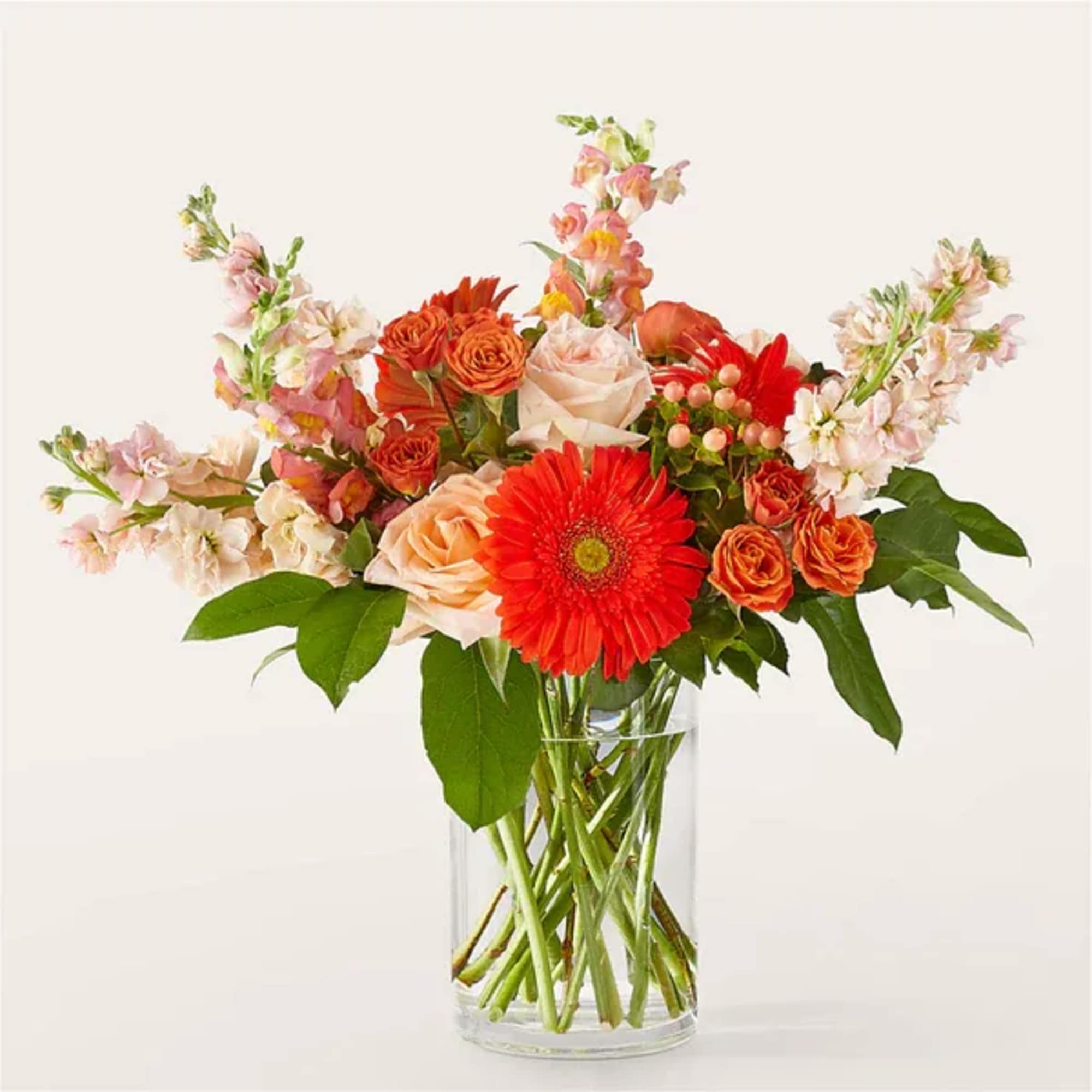 Mixed bouquet of orange and pink flowers in a clear glass vase