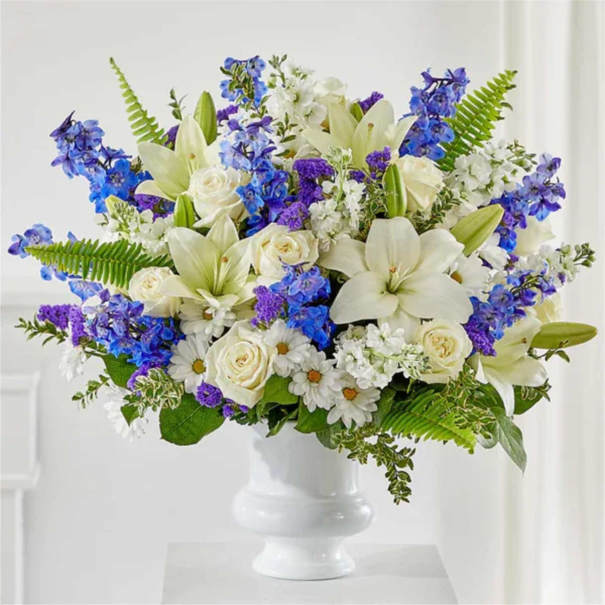 White lilies and roses with blue and purple flowers in a white vase