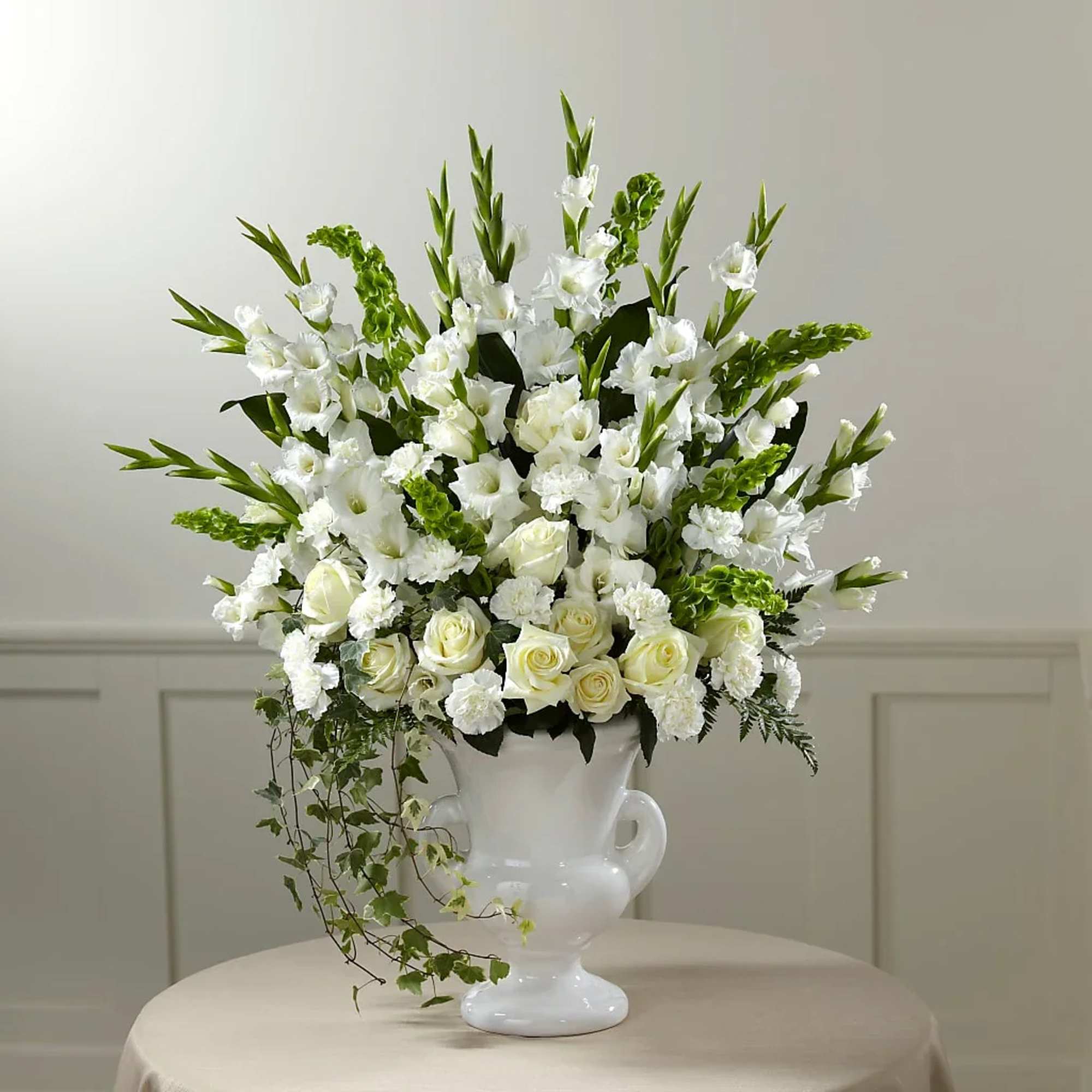 White floral arrangement in a white urn vase with trailing ivy