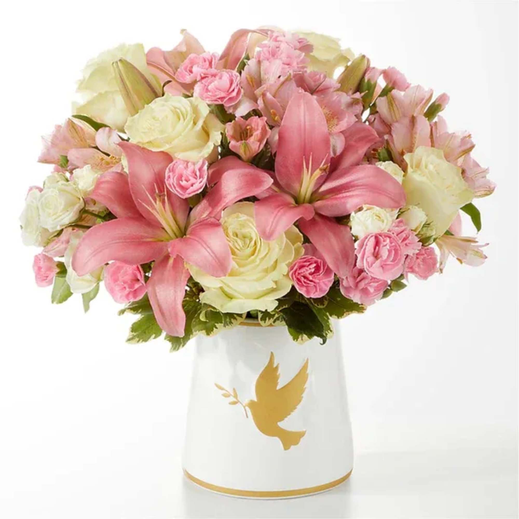 Pink lilies and roses arranged in a white vase with a gold dove design.