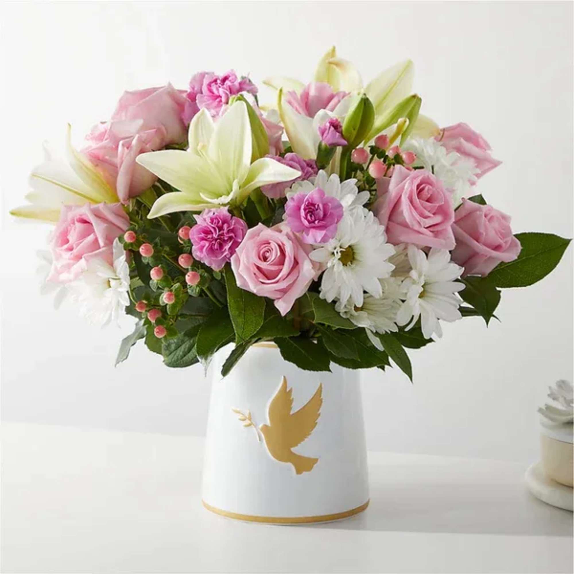 Pink roses and white lilies arranged in a white vase with a gold dove design.