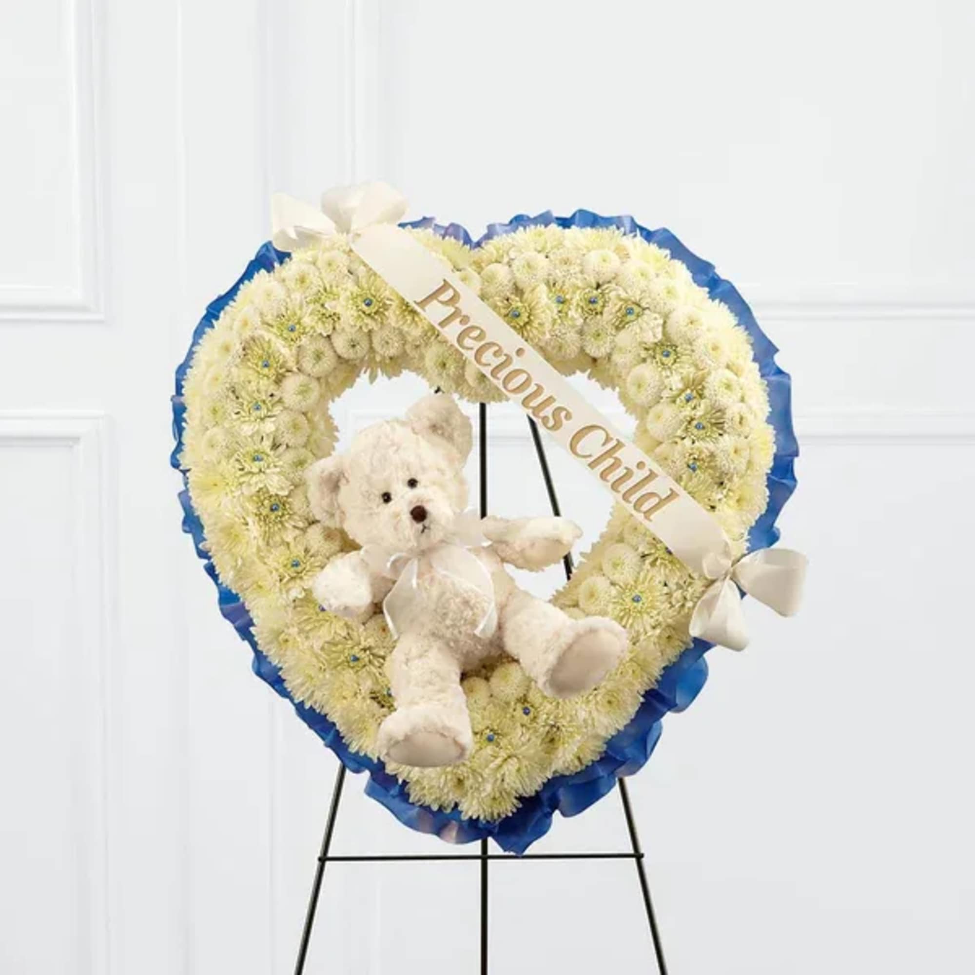 Heart-shaped white floral wreath with a teddy bear and ribbon on an easel