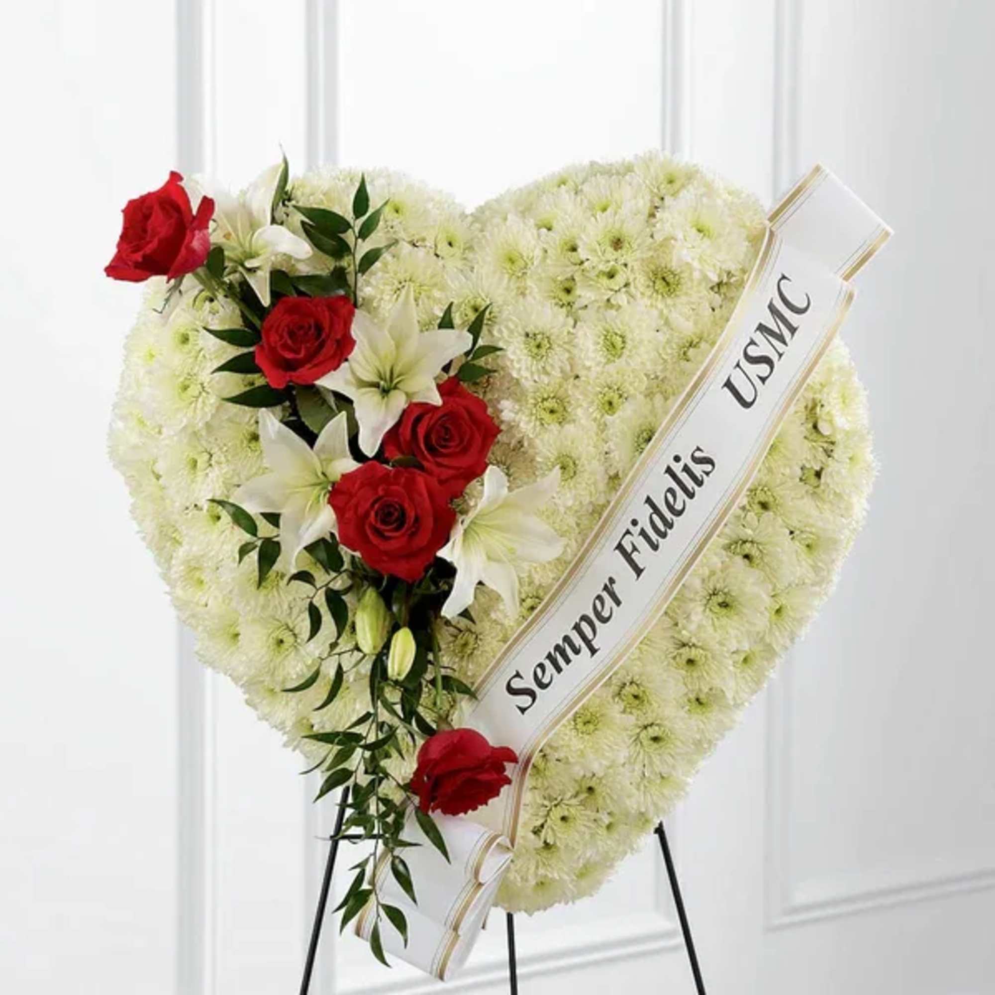Heart-shaped funeral wreath with red roses and white lilies on a stand