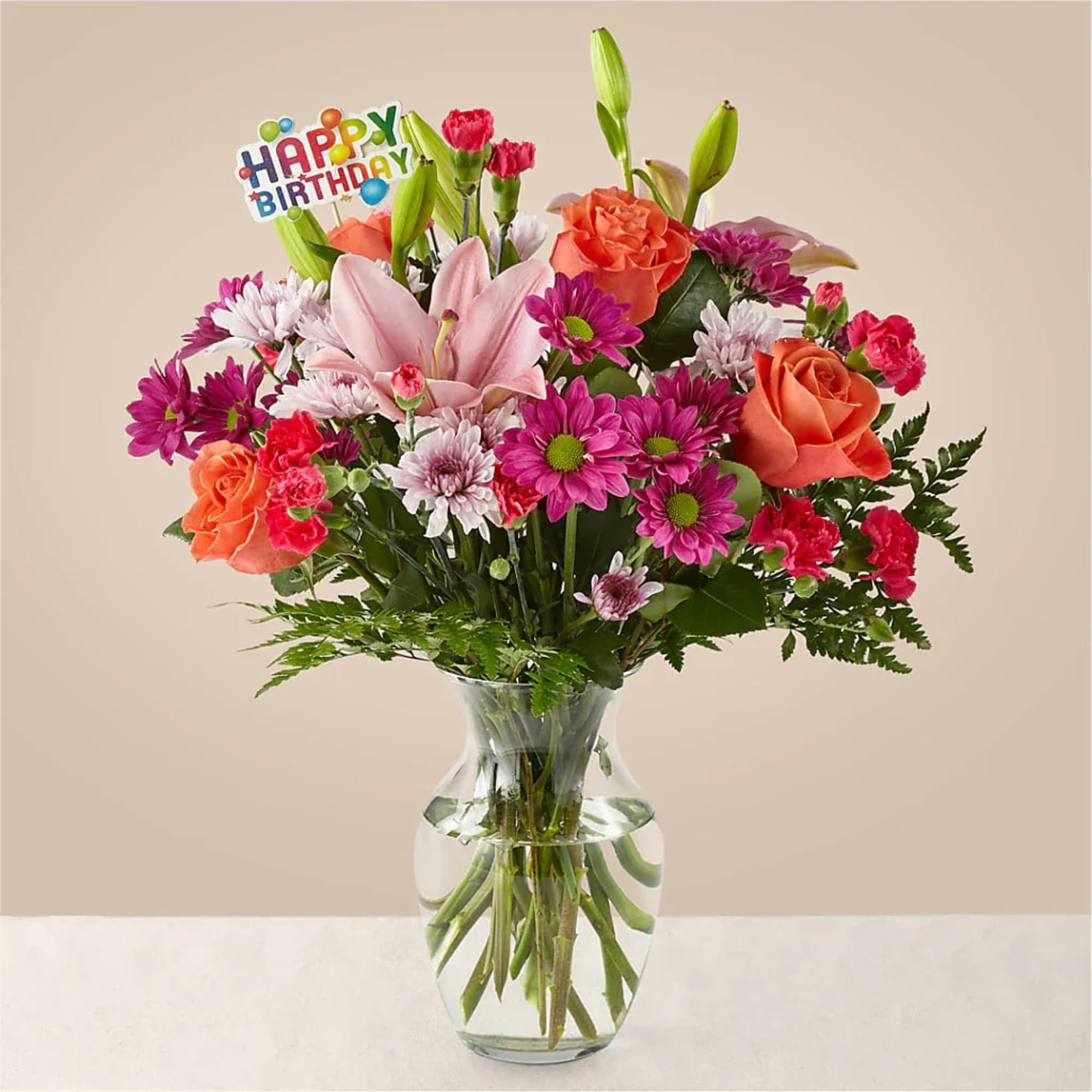 Mixed bouquet of roses, lilies, and daisies in a clear glass vase