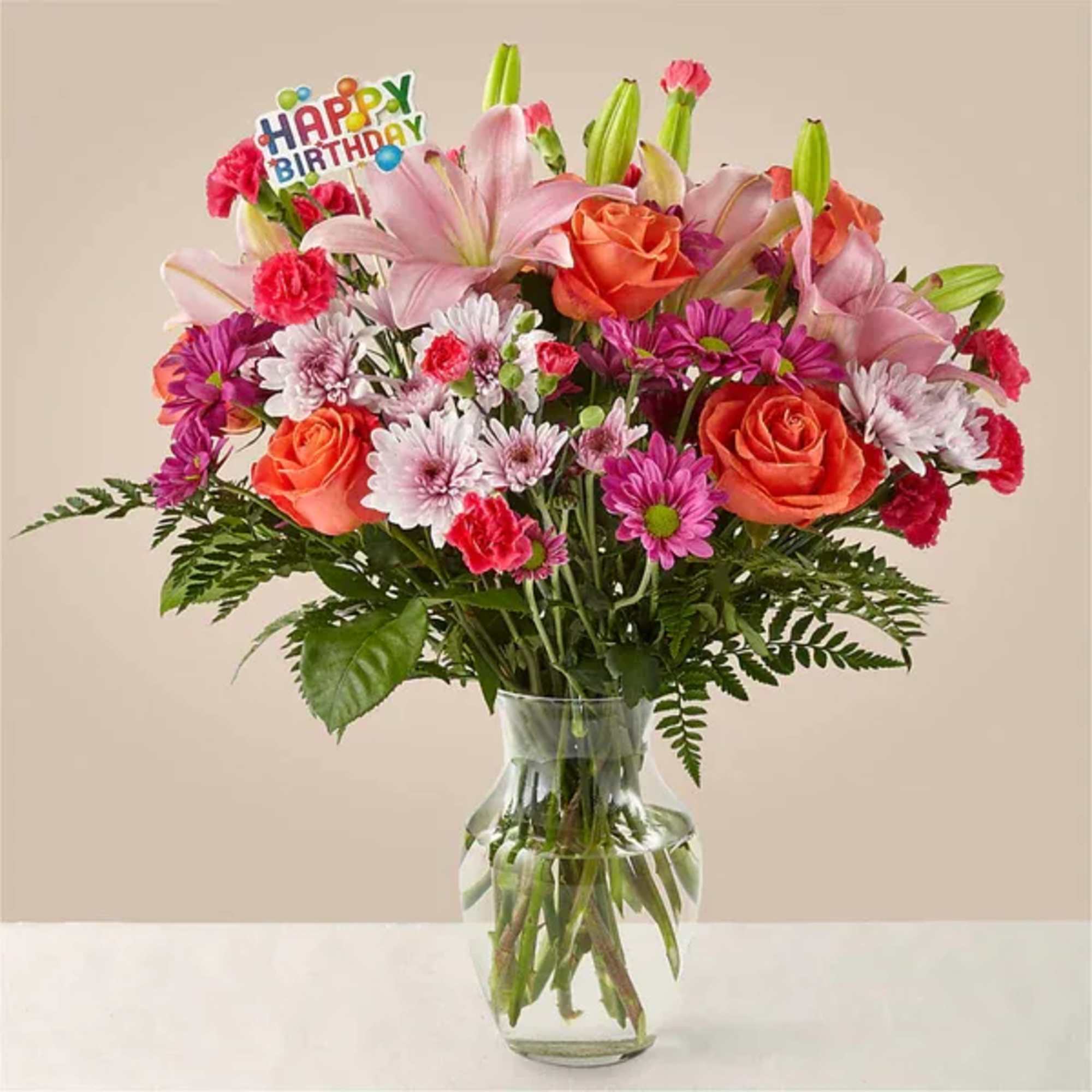 Mixed bouquet of pink lilies, orange roses, and daisies in a glass vase