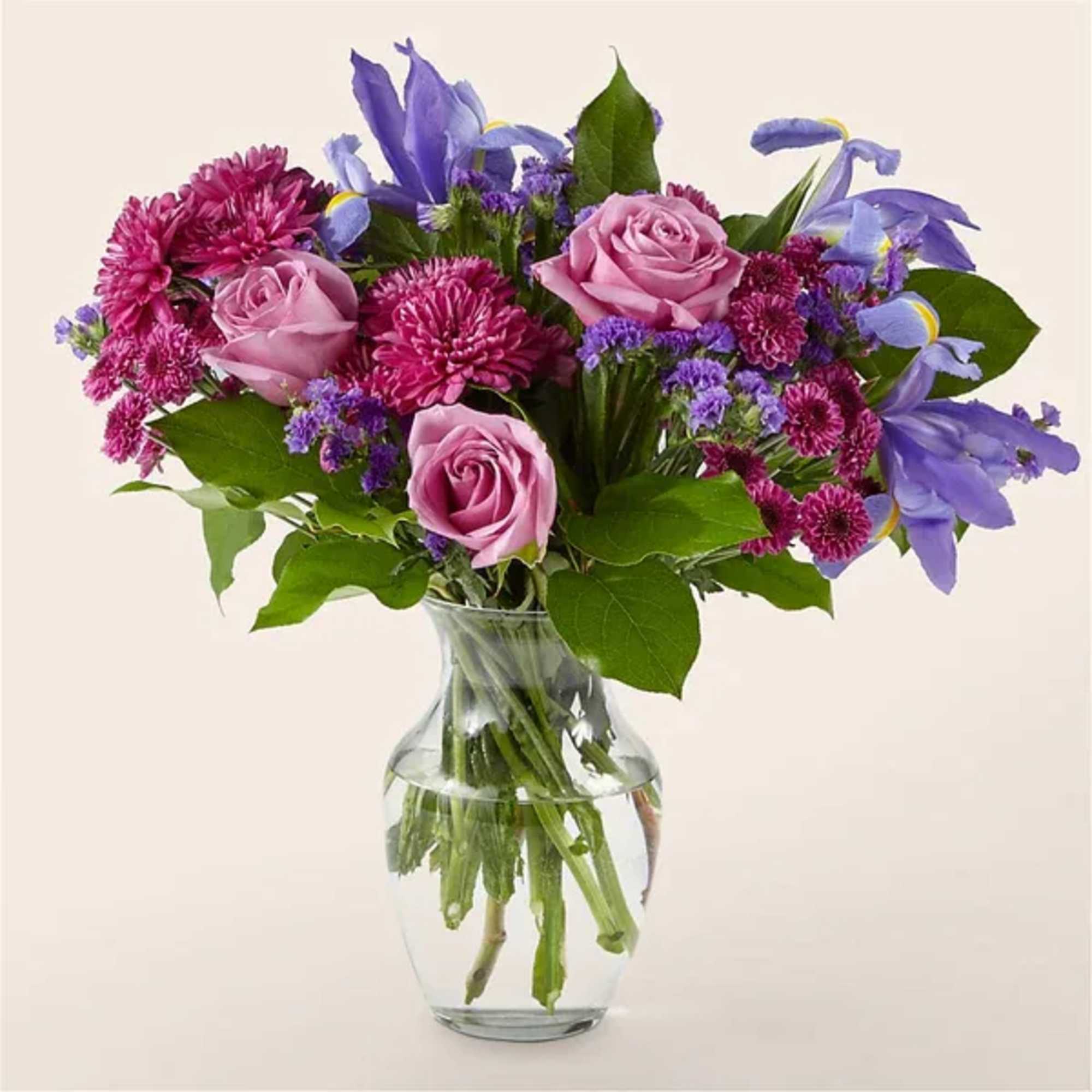 Pink roses and purple flowers arranged in a clear glass vase