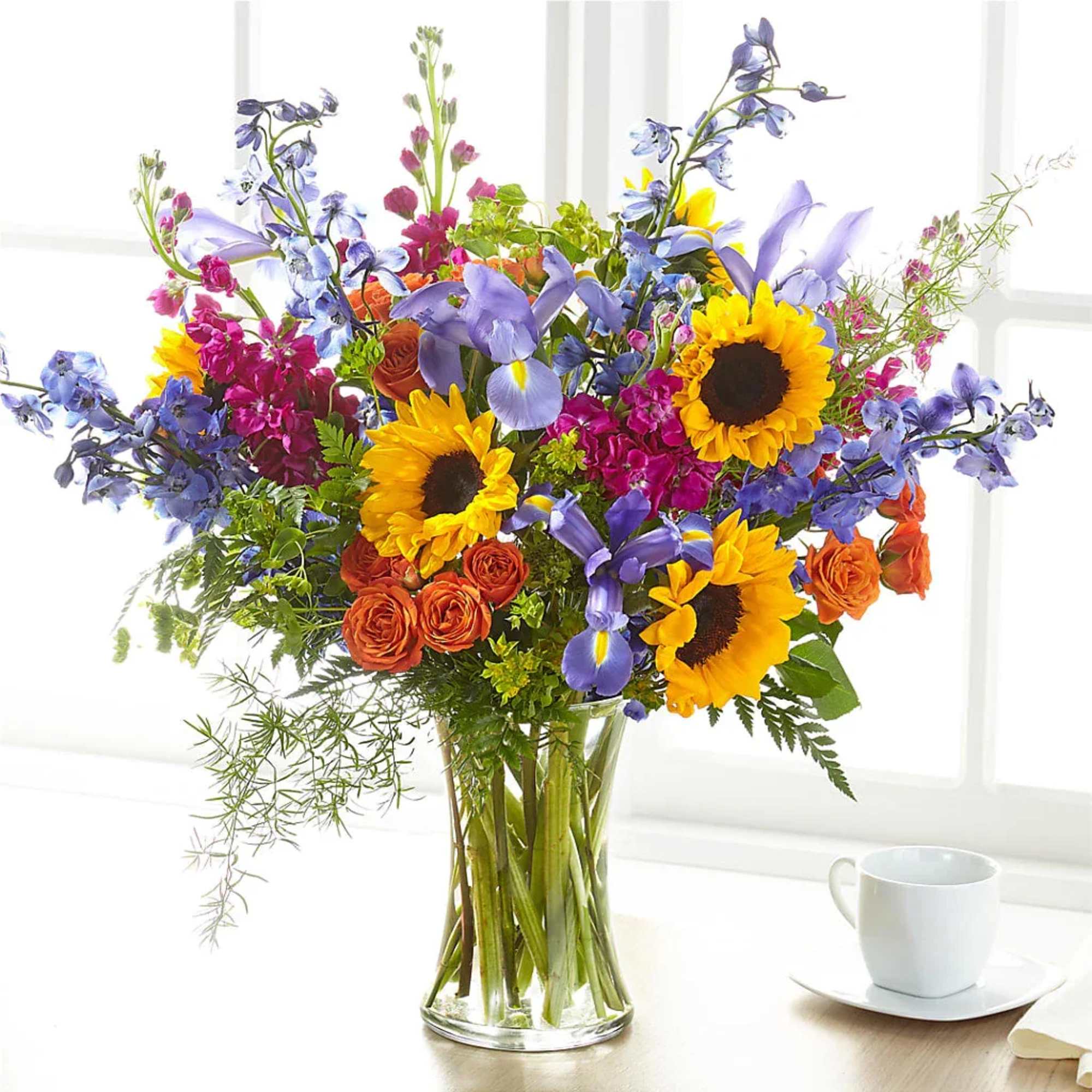 Bright mixed bouquet with sunflowers, purple irises, and orange roses in a glass vase