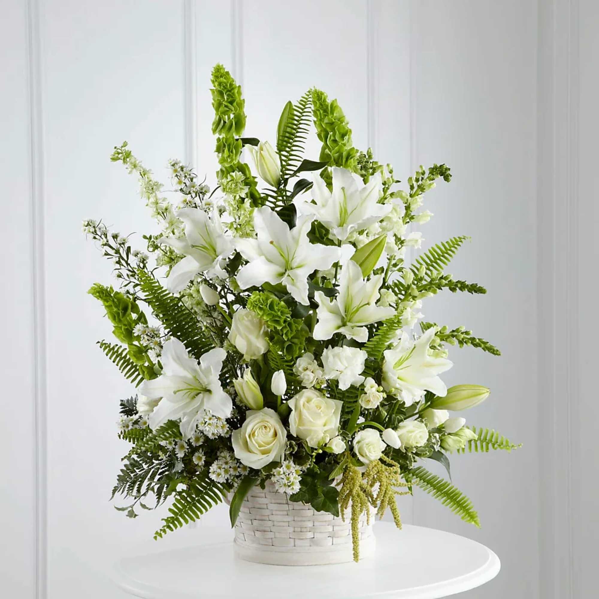 White lilies and roses in a white woven basket with green accents