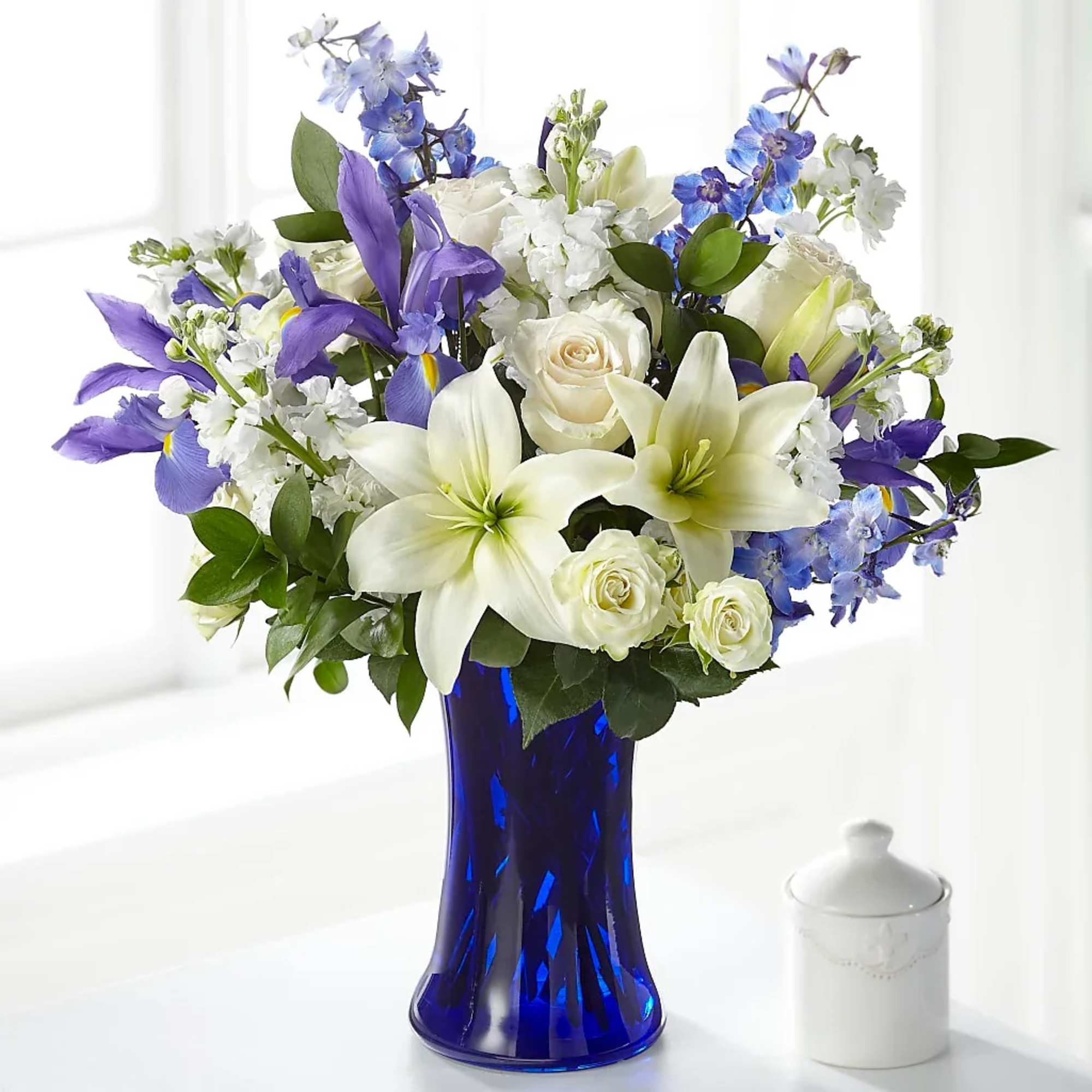 White lilies, roses, and blue flowers in a cobalt vase