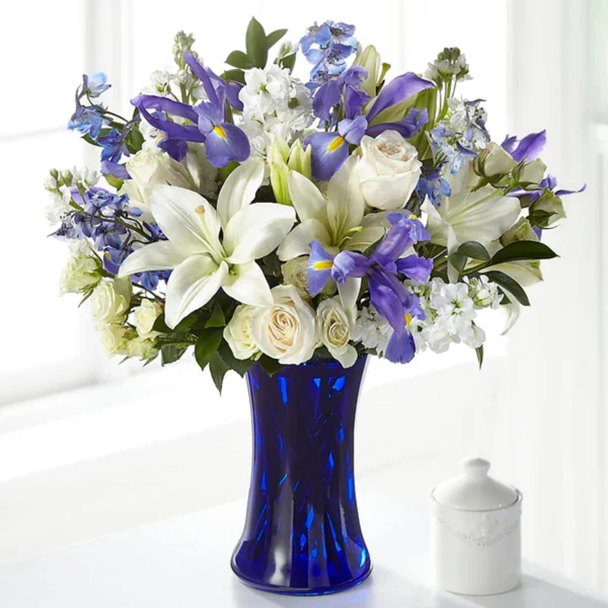 White lilies and purple iris in a blue glass vase
