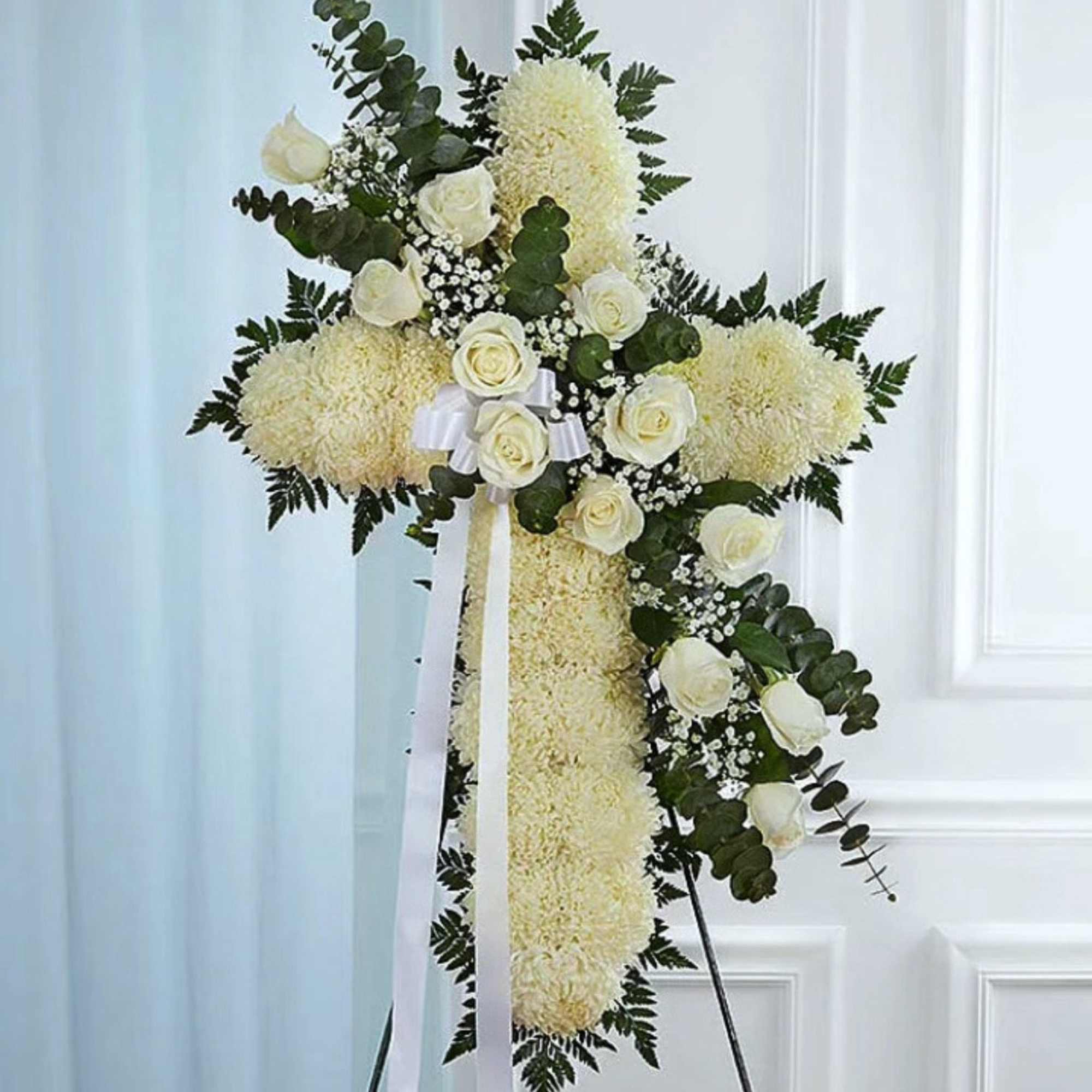 White floral standing cross with roses and ribbon on an easel