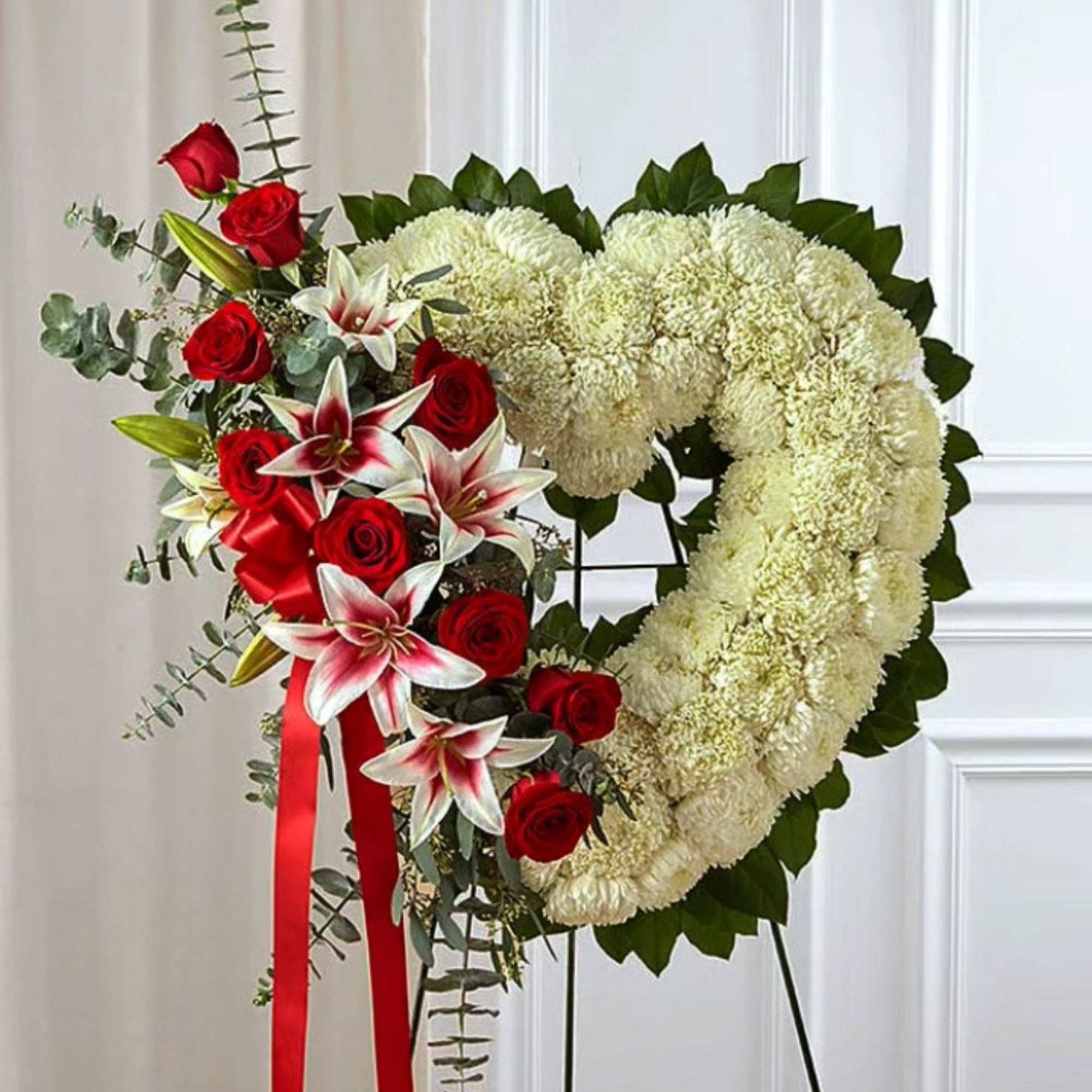 Heart-shaped floral wreath with red roses and white lilies on an easel