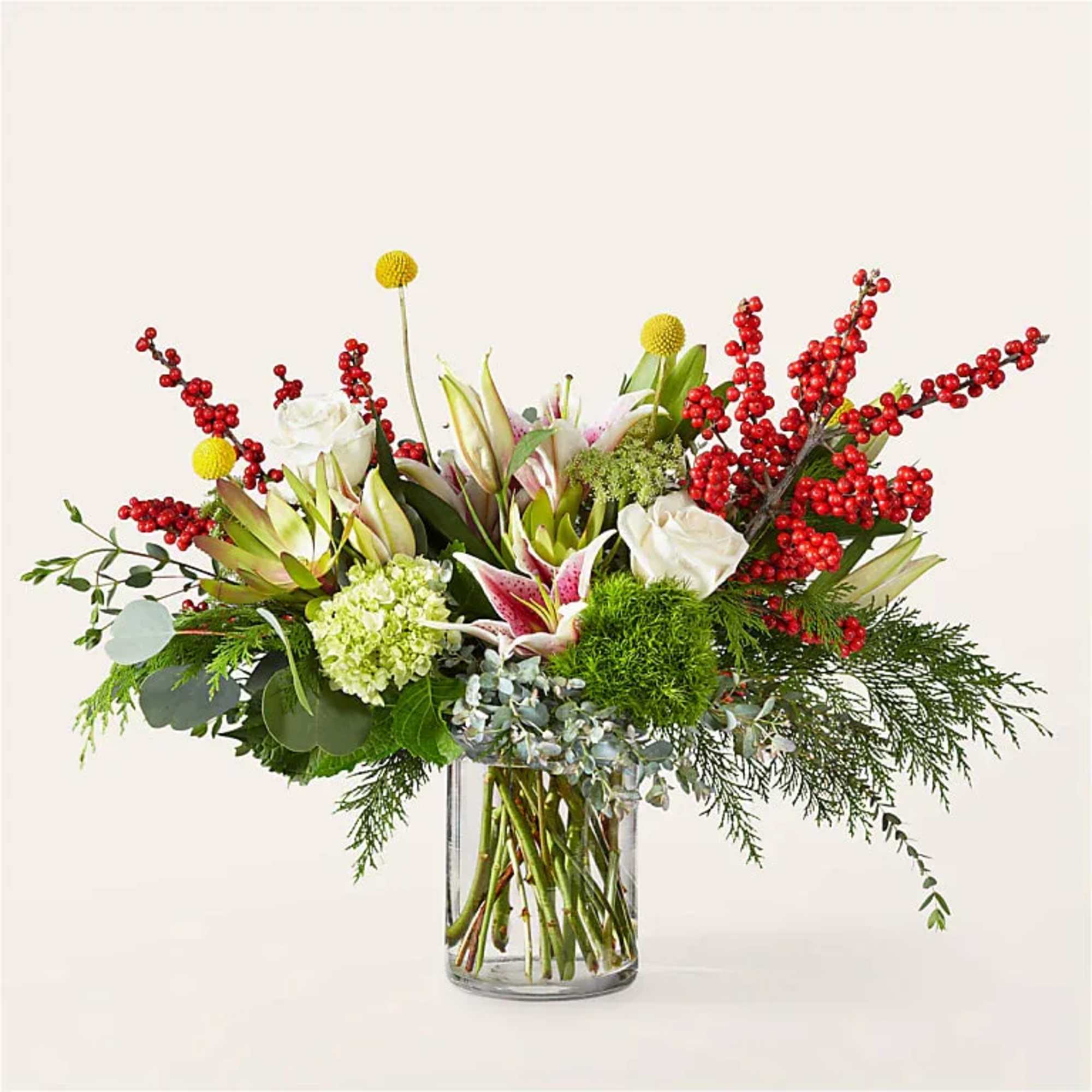 Mixed floral arrangement in a clear glass vase with red berry branches