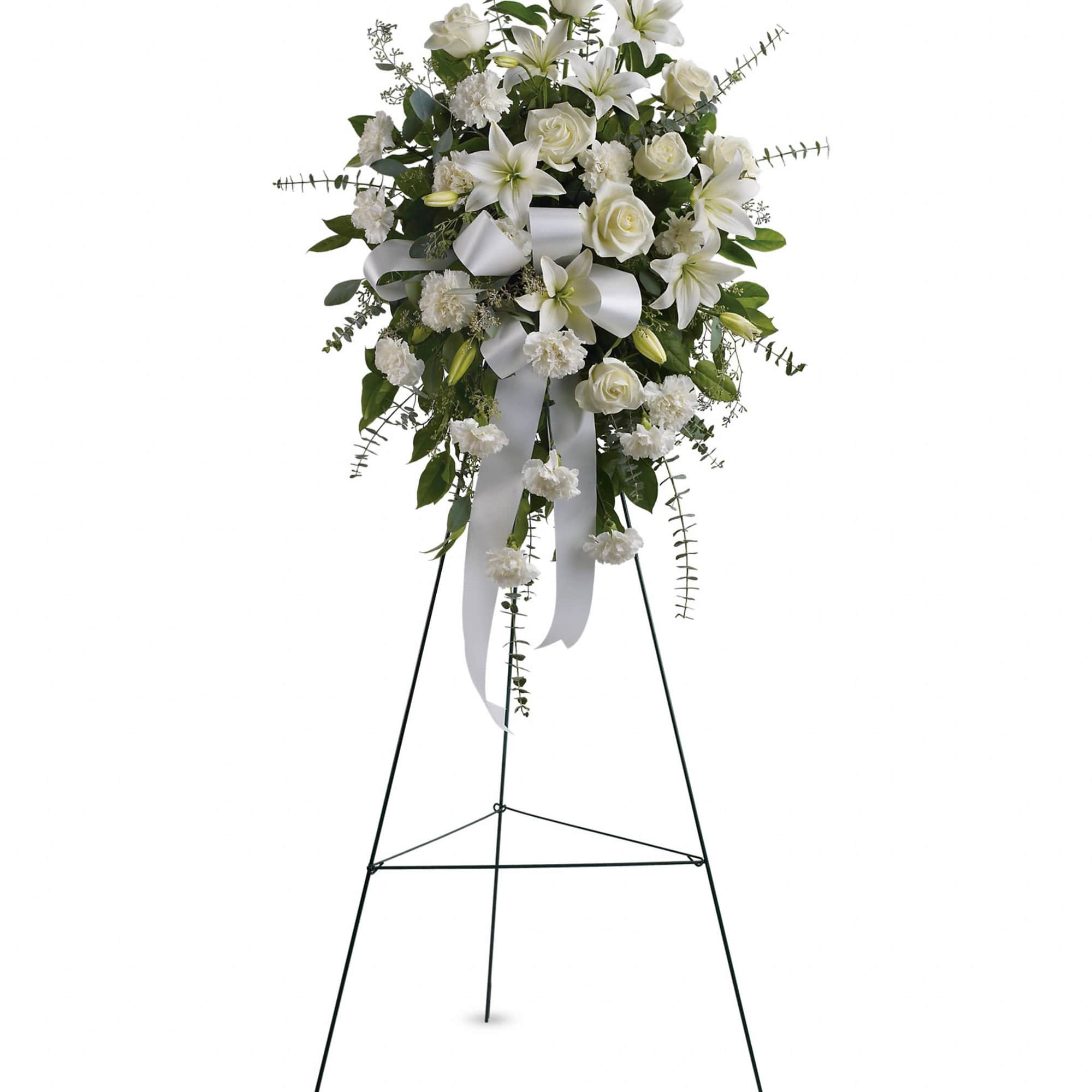 Tall white standing spray with roses, lilies, and carnations on a metal easel with a white ribbon bow