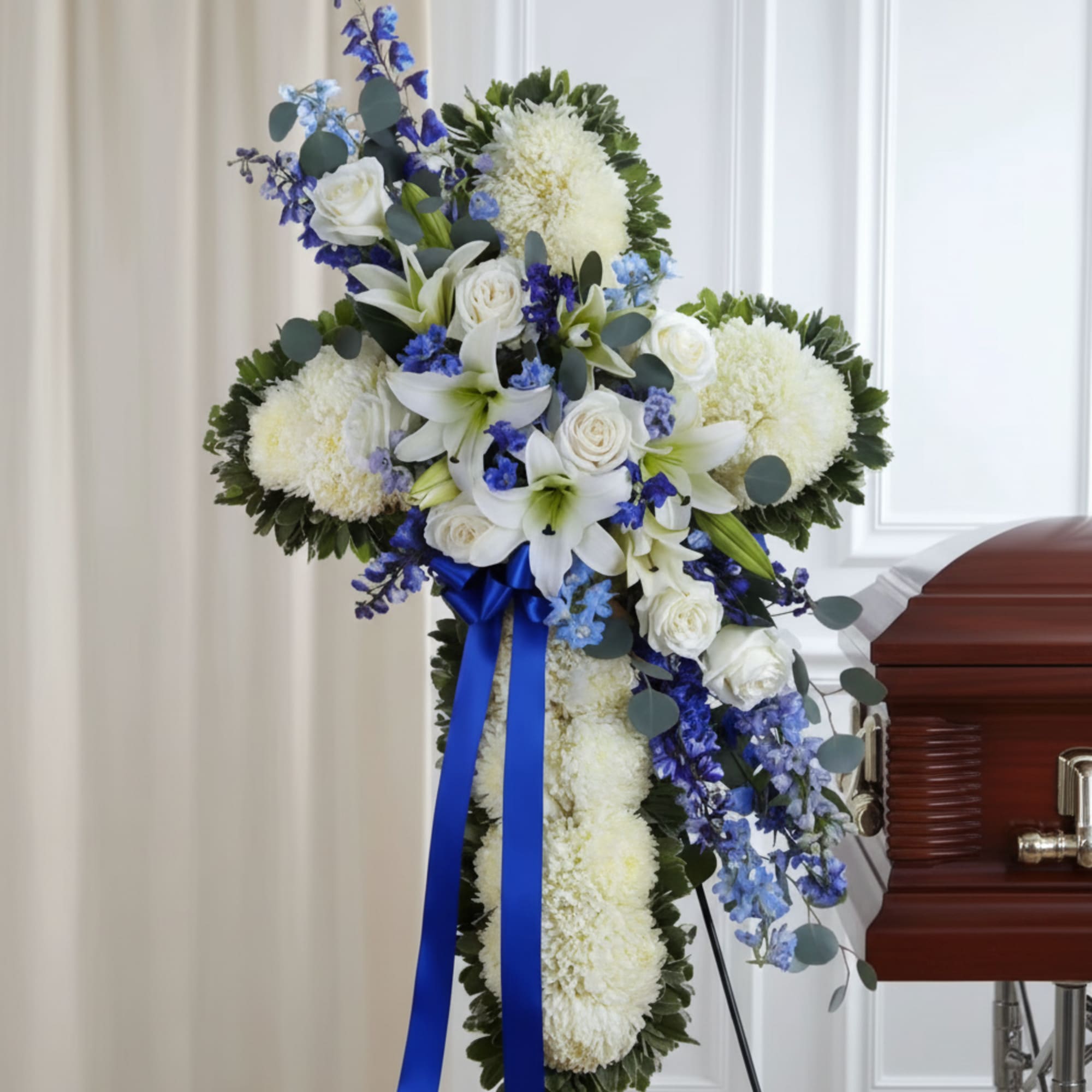 White and blue funeral spray with lilies and roses on a stand