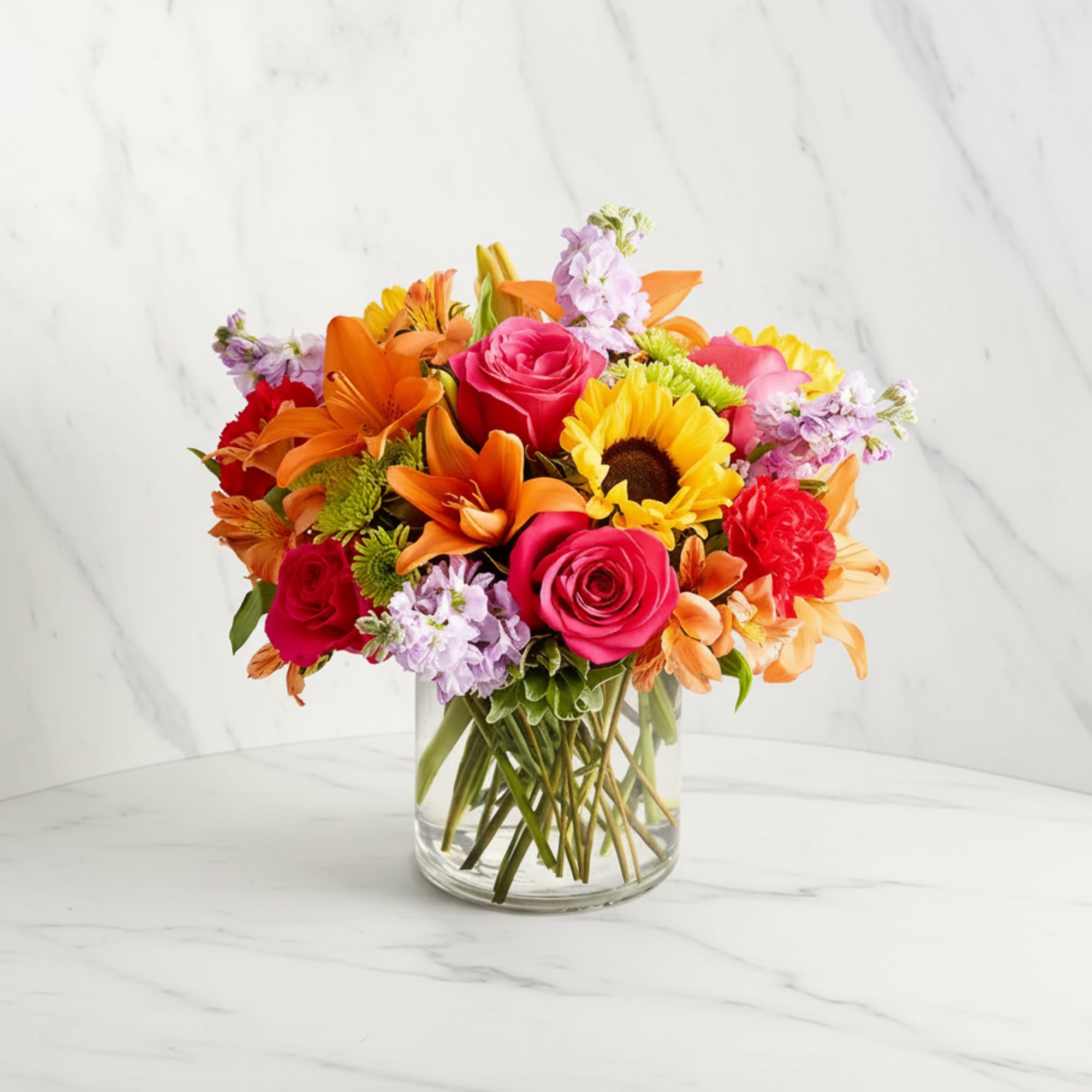 Mixed bouquet of roses, lilies, sunflowers, and carnations in a clear glass vase