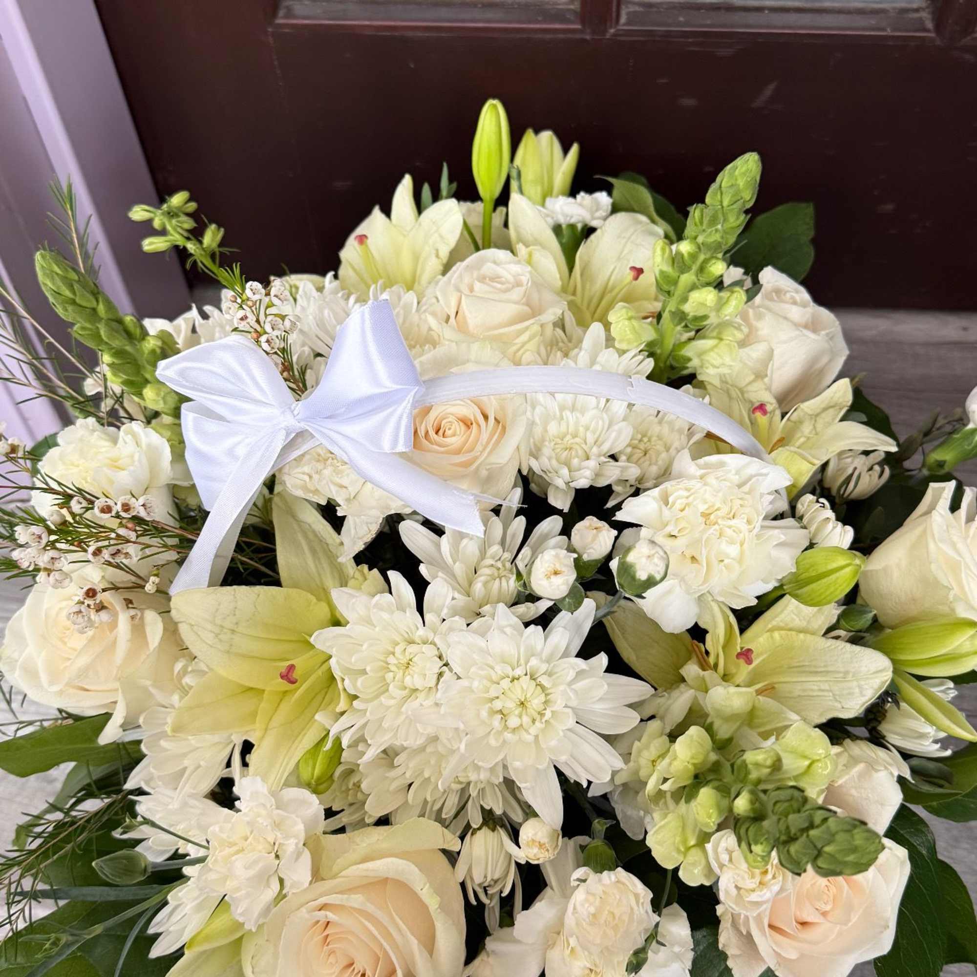 Cream bouquet with roses, lilies, and white blooms tied with a white ribbon