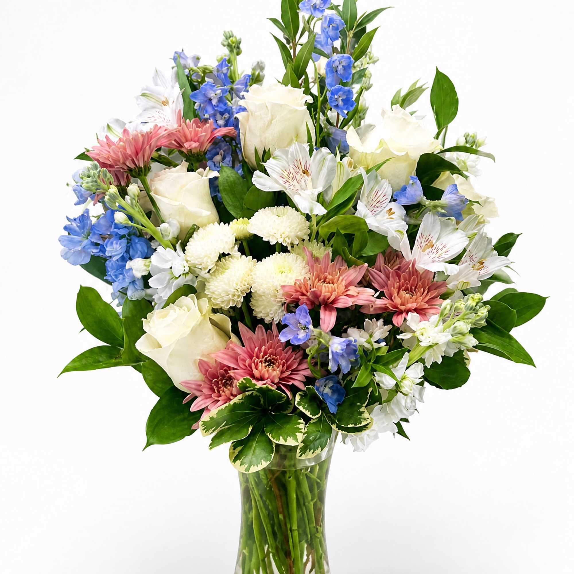 Mixed bouquet of white roses, blue flowers, and pink daisies in a glass vase
