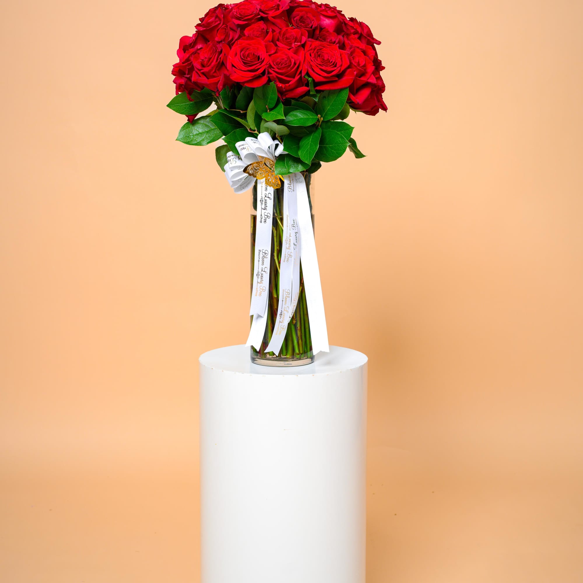 Tall bouquet of red roses in a glass vase with white ribbons