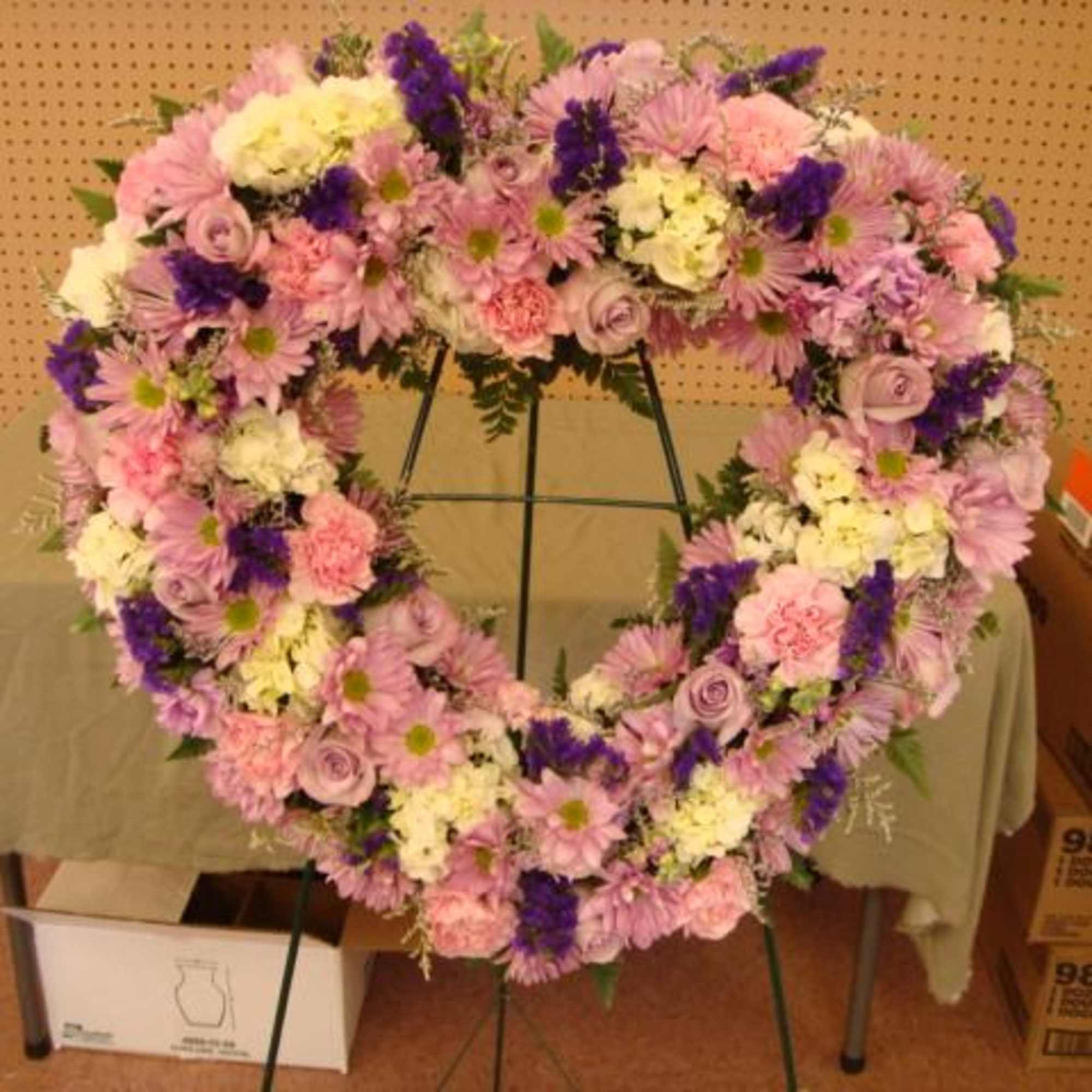 Heart-shaped floral wreath with pink, white, and purple flowers on a stand