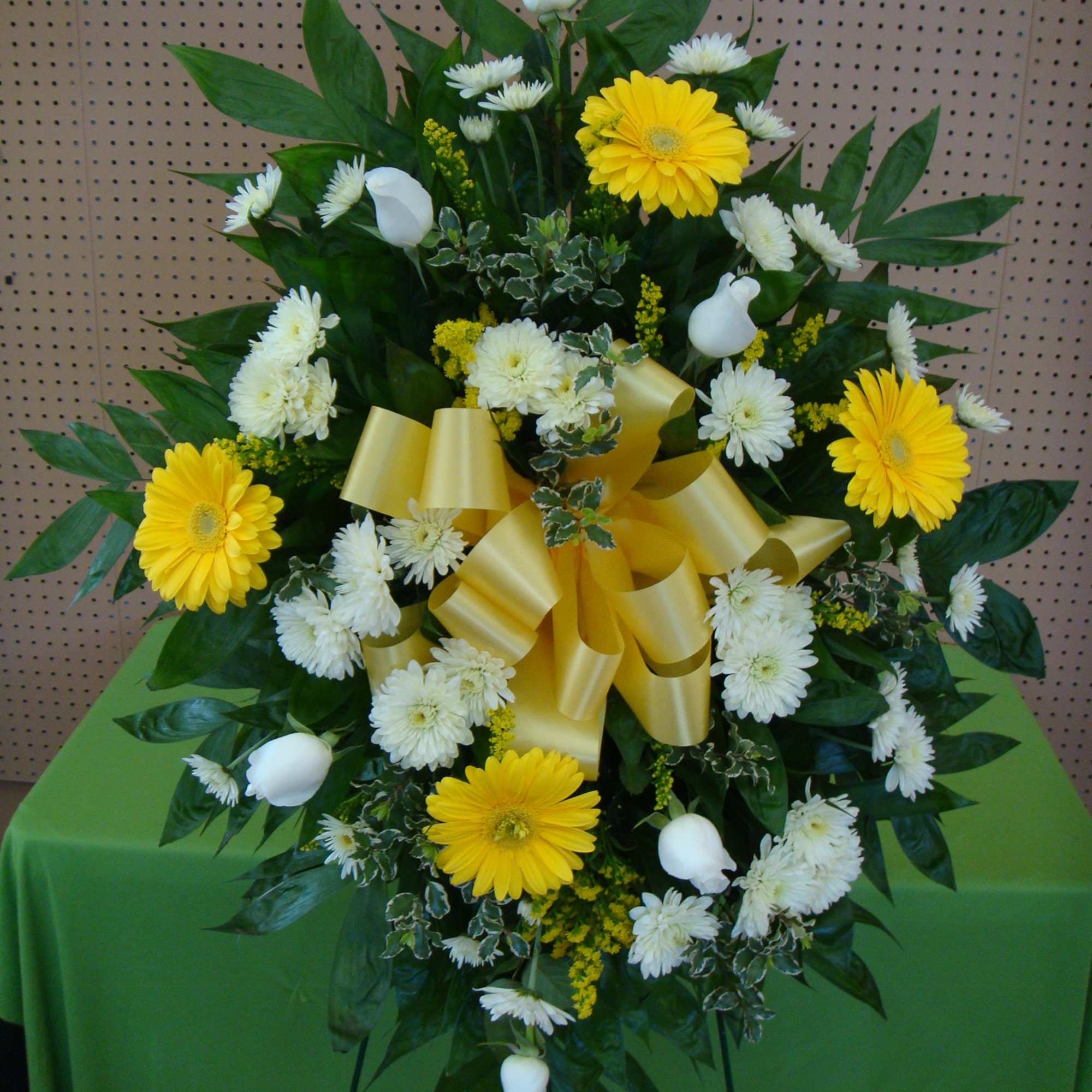 Standing floral spray with yellow gerbera daisies and white blooms, finished with a gold bow