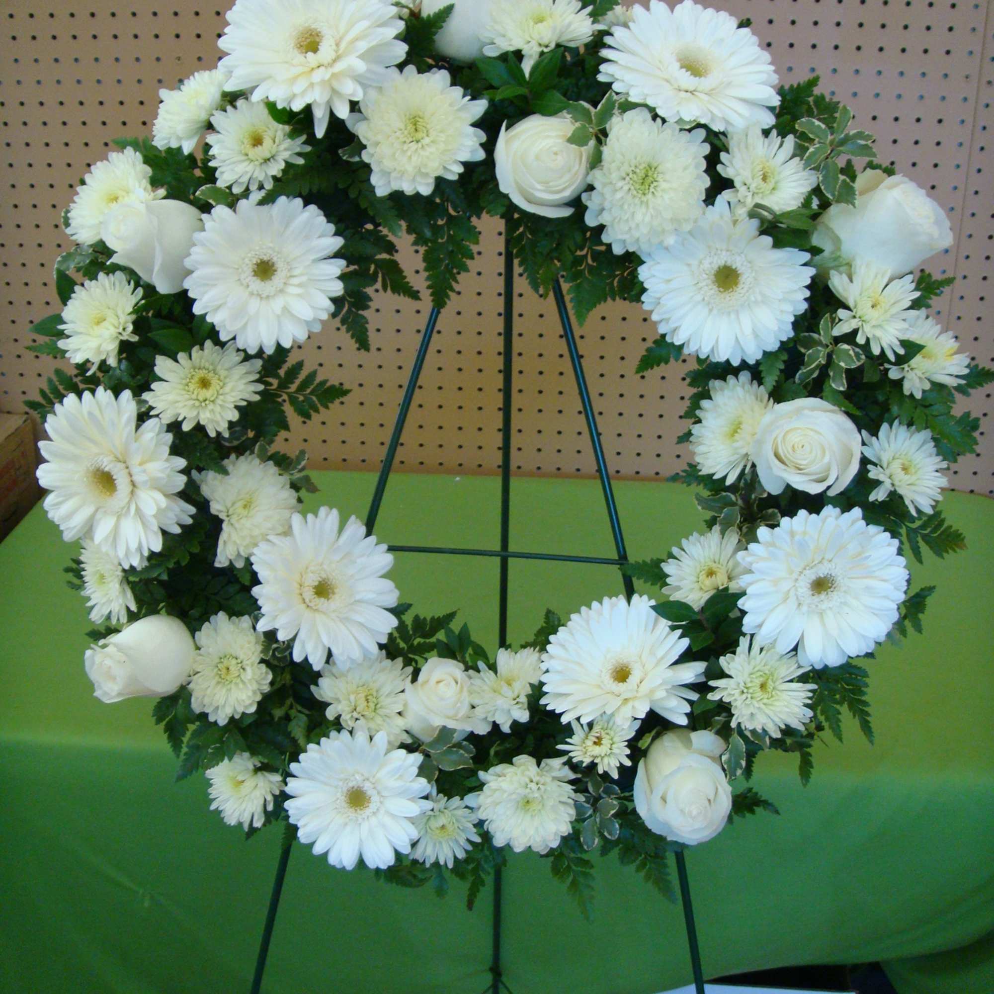 White floral wreath on a stand with roses and daisy-like blooms