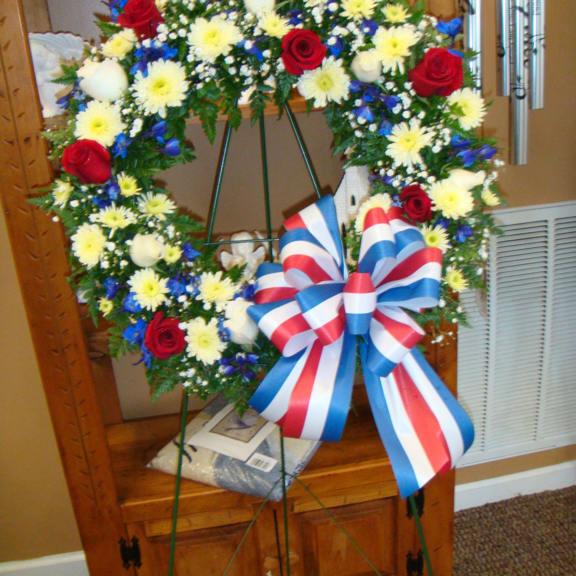 Circular funeral wreath with red roses, white daisies, and a red-white-blue bow
